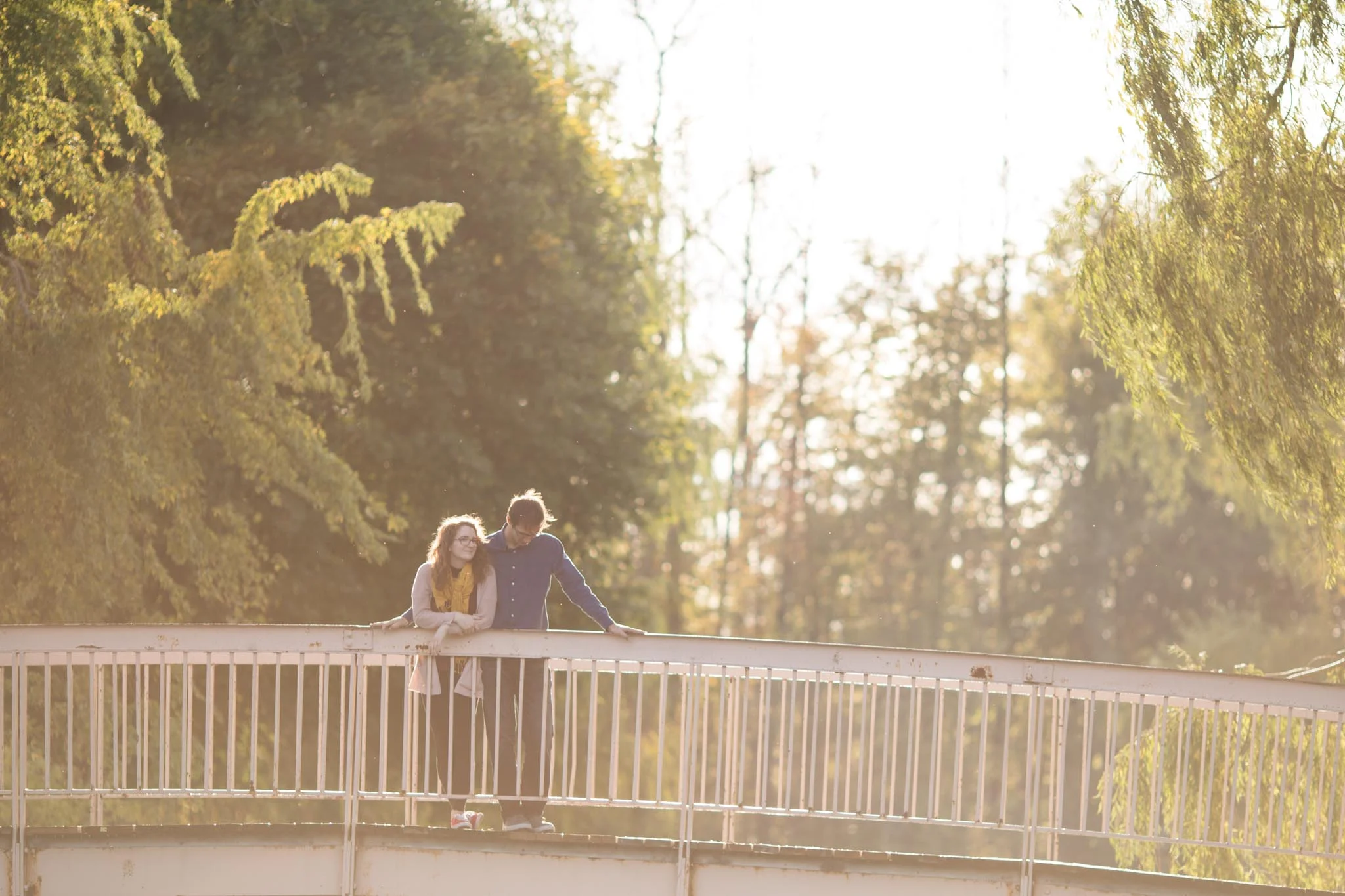 couple standing on a bridge with red converse and willow trees couple photography session in Victoria Park Kitchener Ontario.jpg