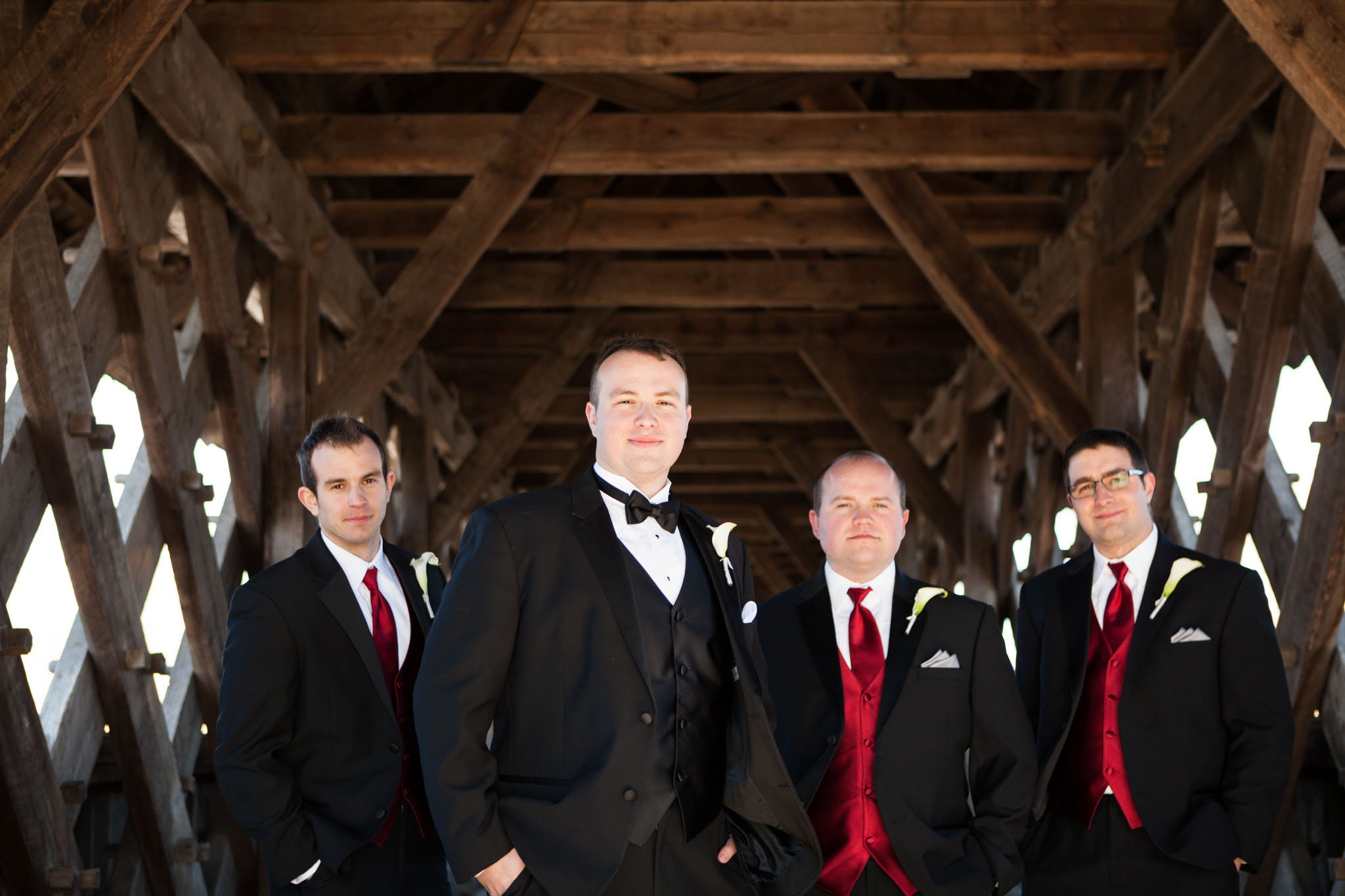 groom and groomsmen portrait red vests on wood covered bridge.jpg
