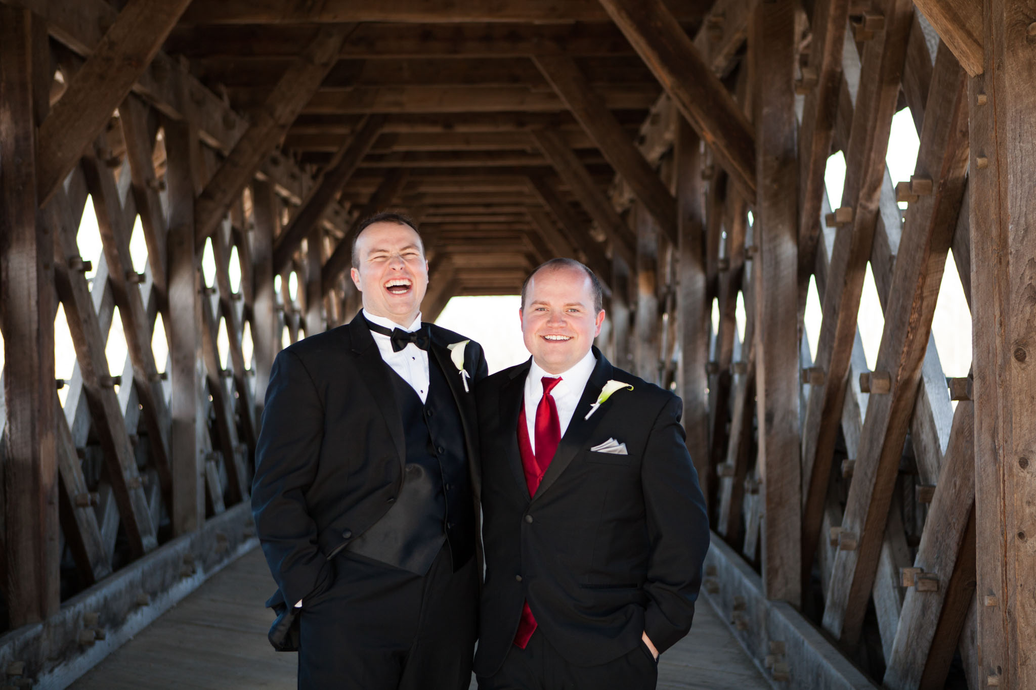 groom laughing with groomsman on covered wood bridge.jpg