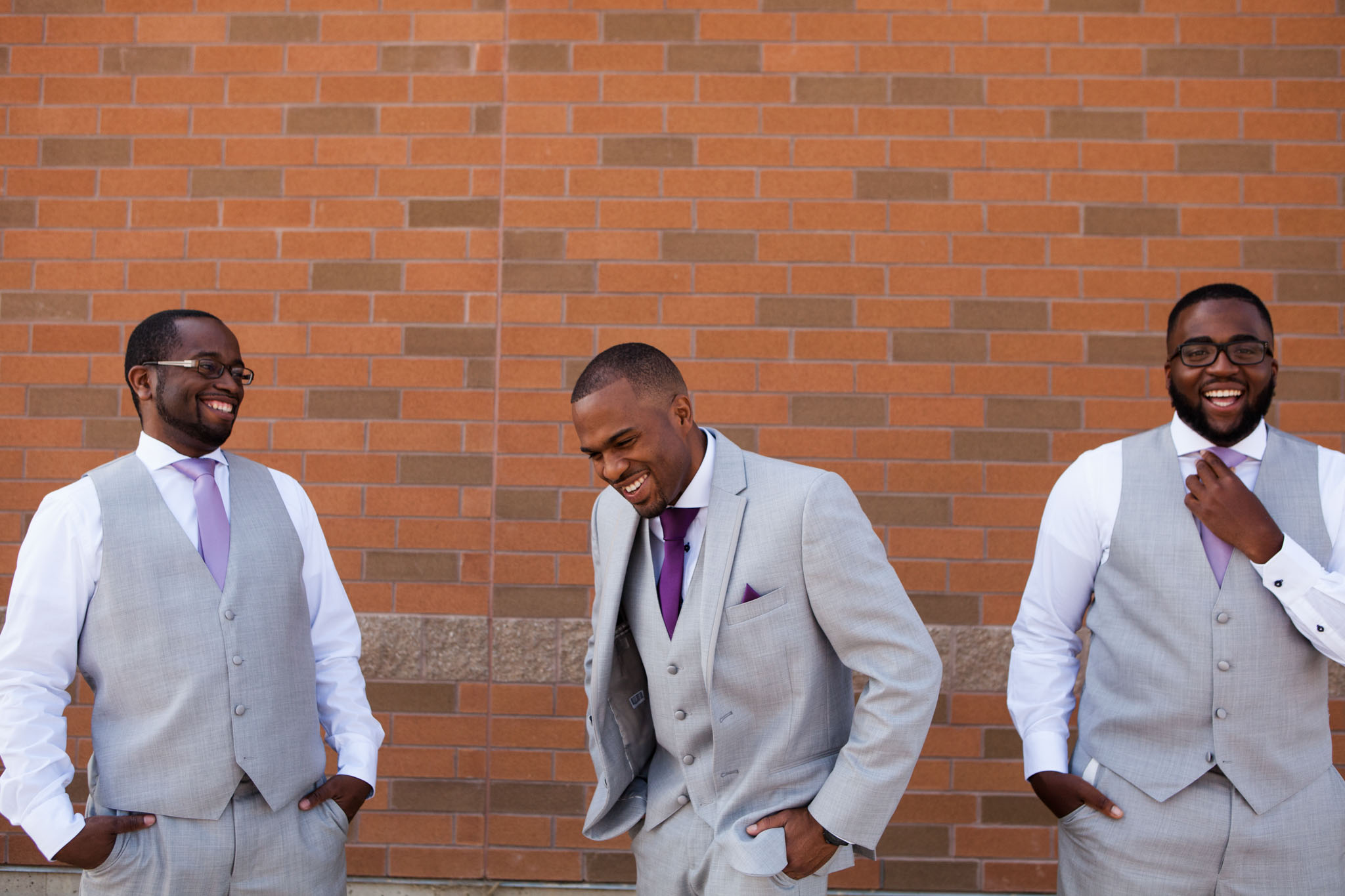 wedding photography groom and groomsmen laughing with a red brick wall.jpg
