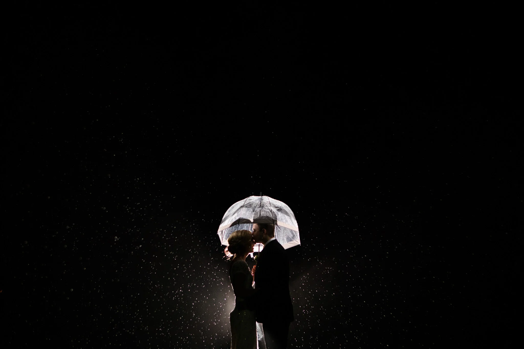 back lit rain portrait of groom kissing bride under a clear umbrella at Polski Dom.jpg