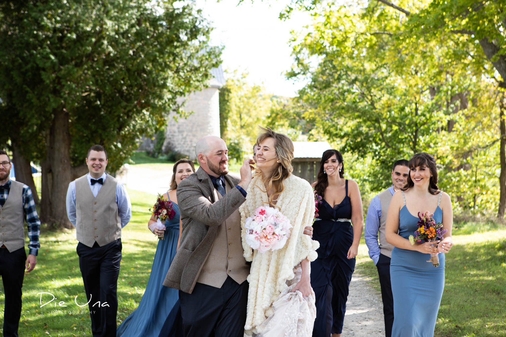 groom fixing brides hair on windy wedding day wedding party in the background walking.jpg