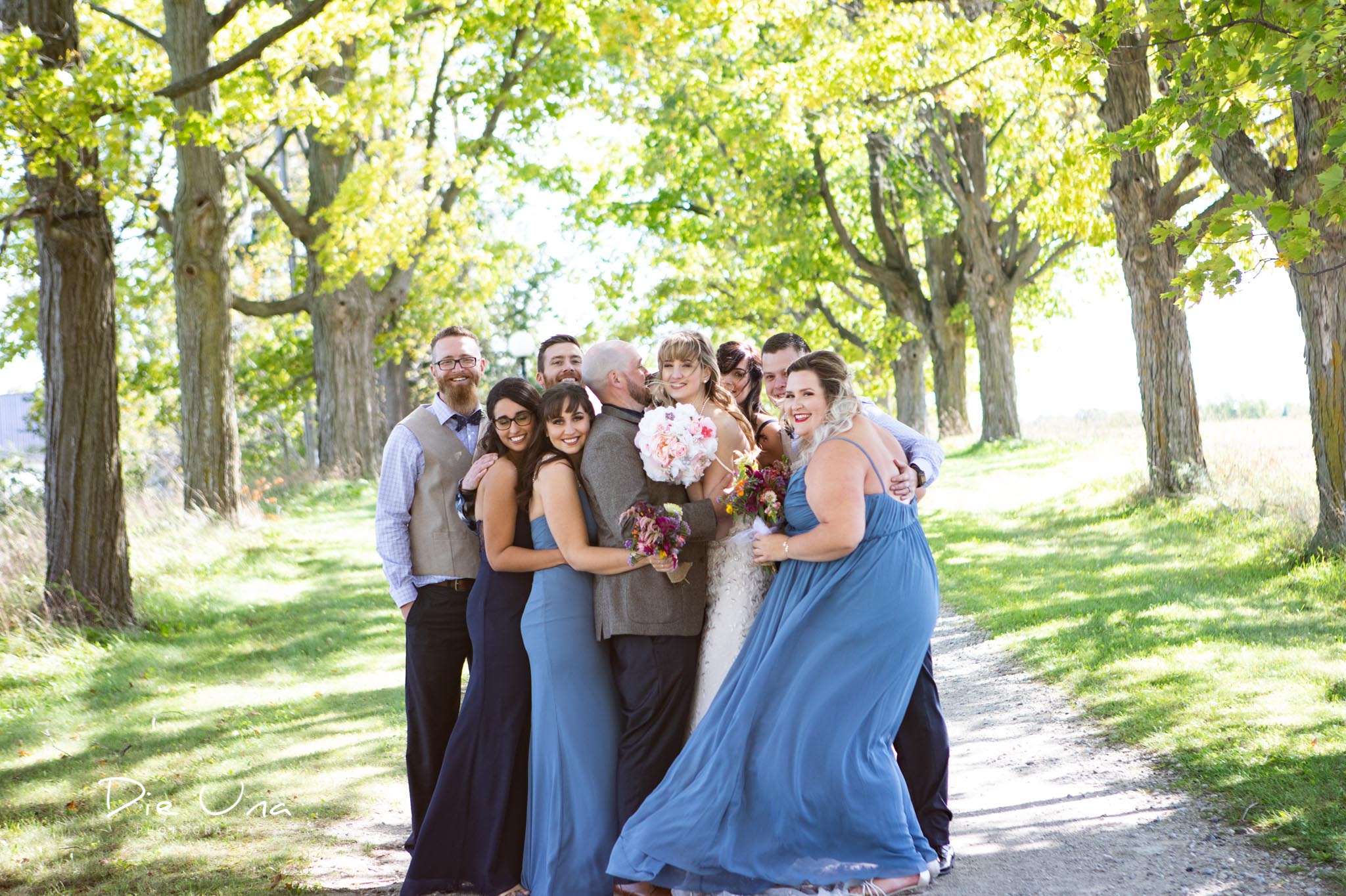 wedding party giving bride and groom a group hug on tree lined driveway.jpg