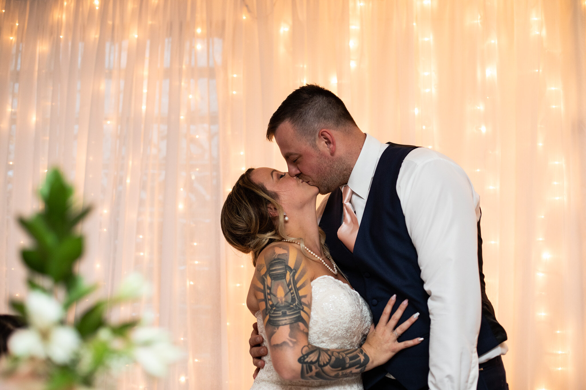 bride and groom kiss at head table with lights behind them.jpg