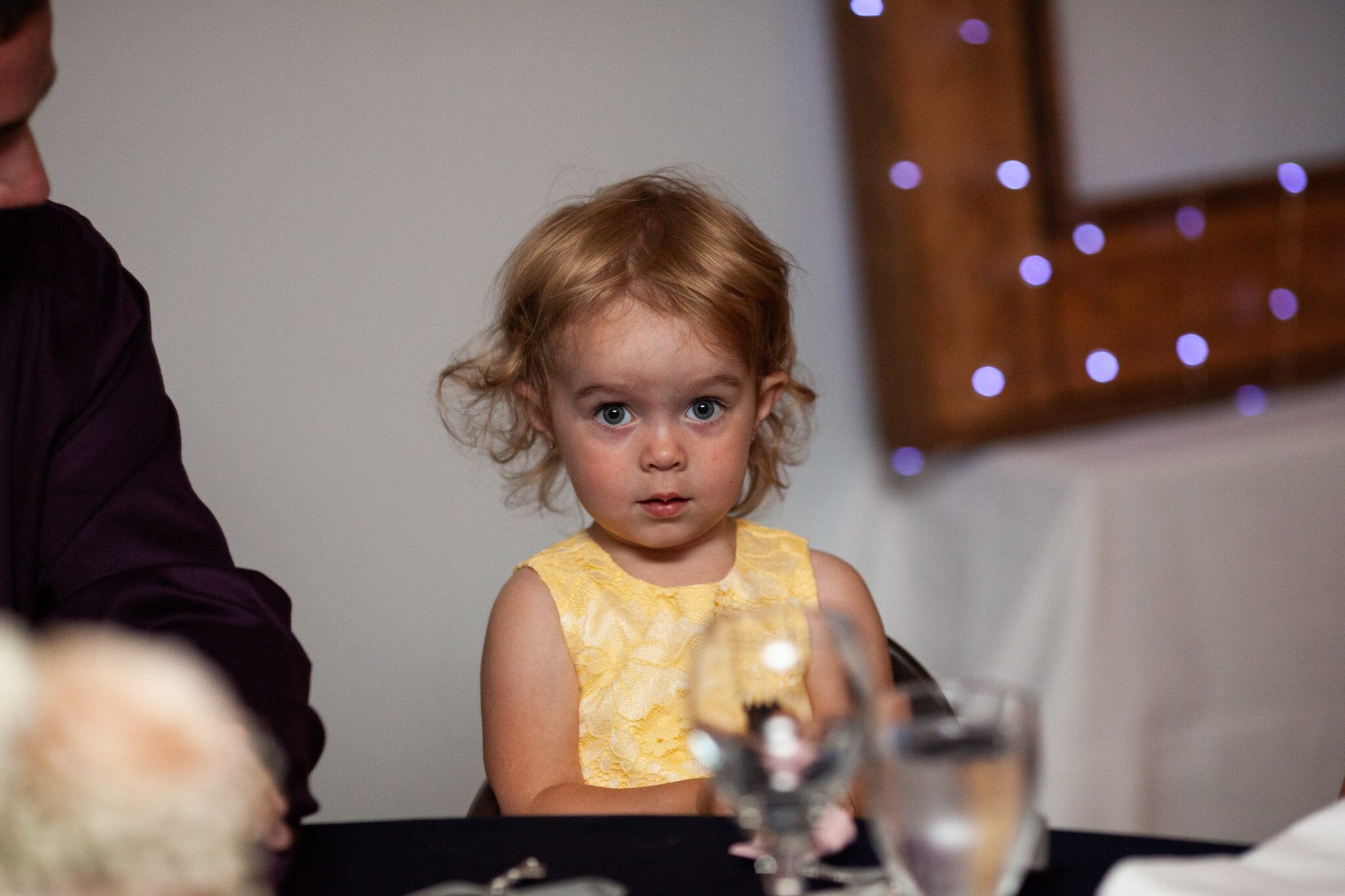 little girl in yellow dress wedding guest sitting at table.jpg