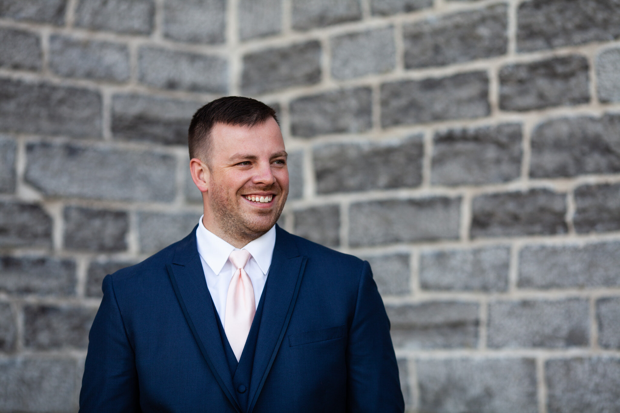 portrait of the groom looking towards the bride with stone wall in the background.jpg