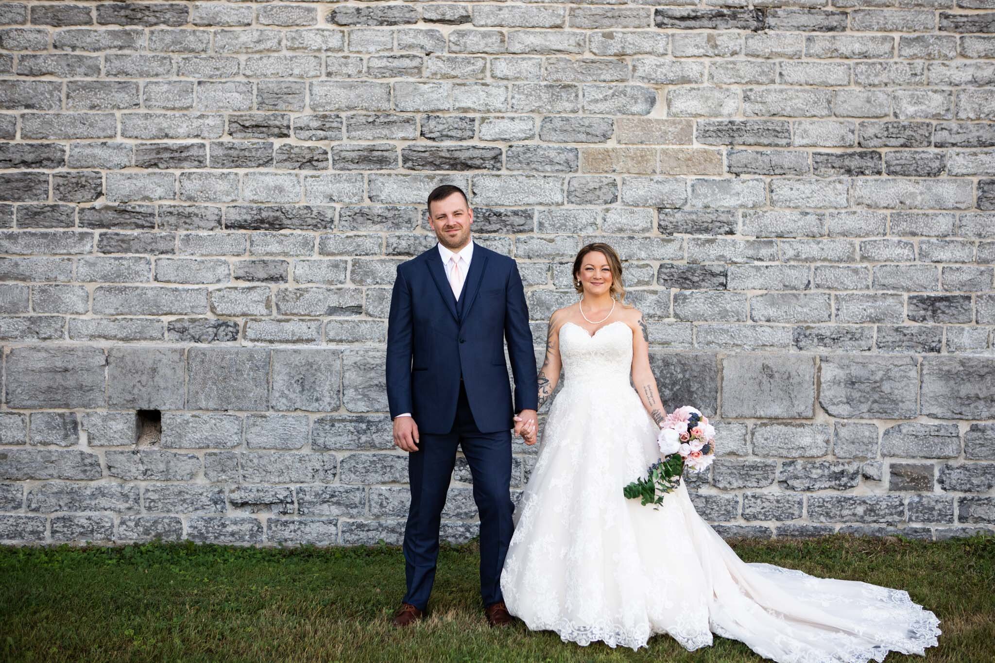 simple bride and groom portrait holding hands in front of a stone wall.jpg