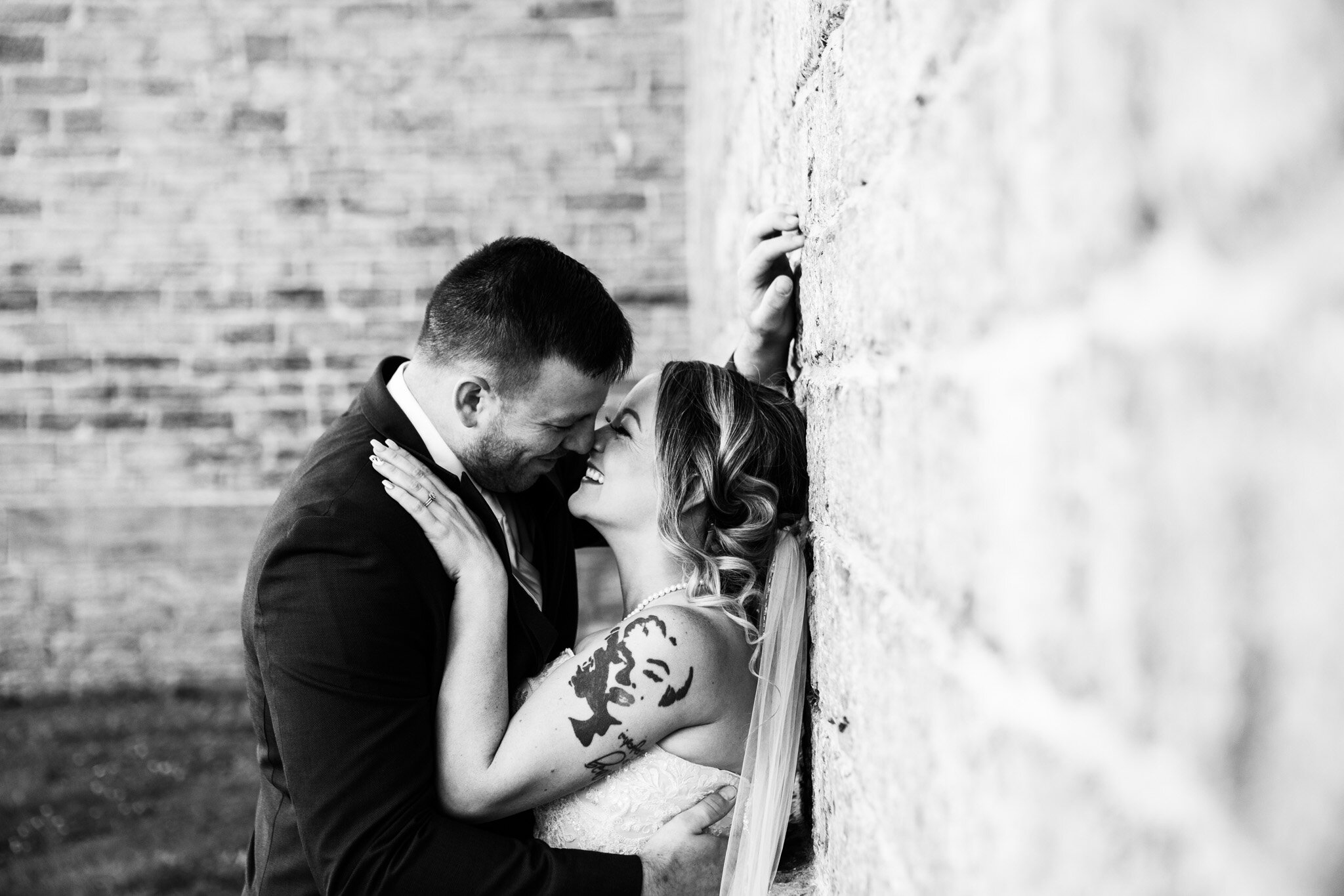 tattooed bride and groom about to kiss leaning against stone wall at St Raphael's ruins in black and white.jpg