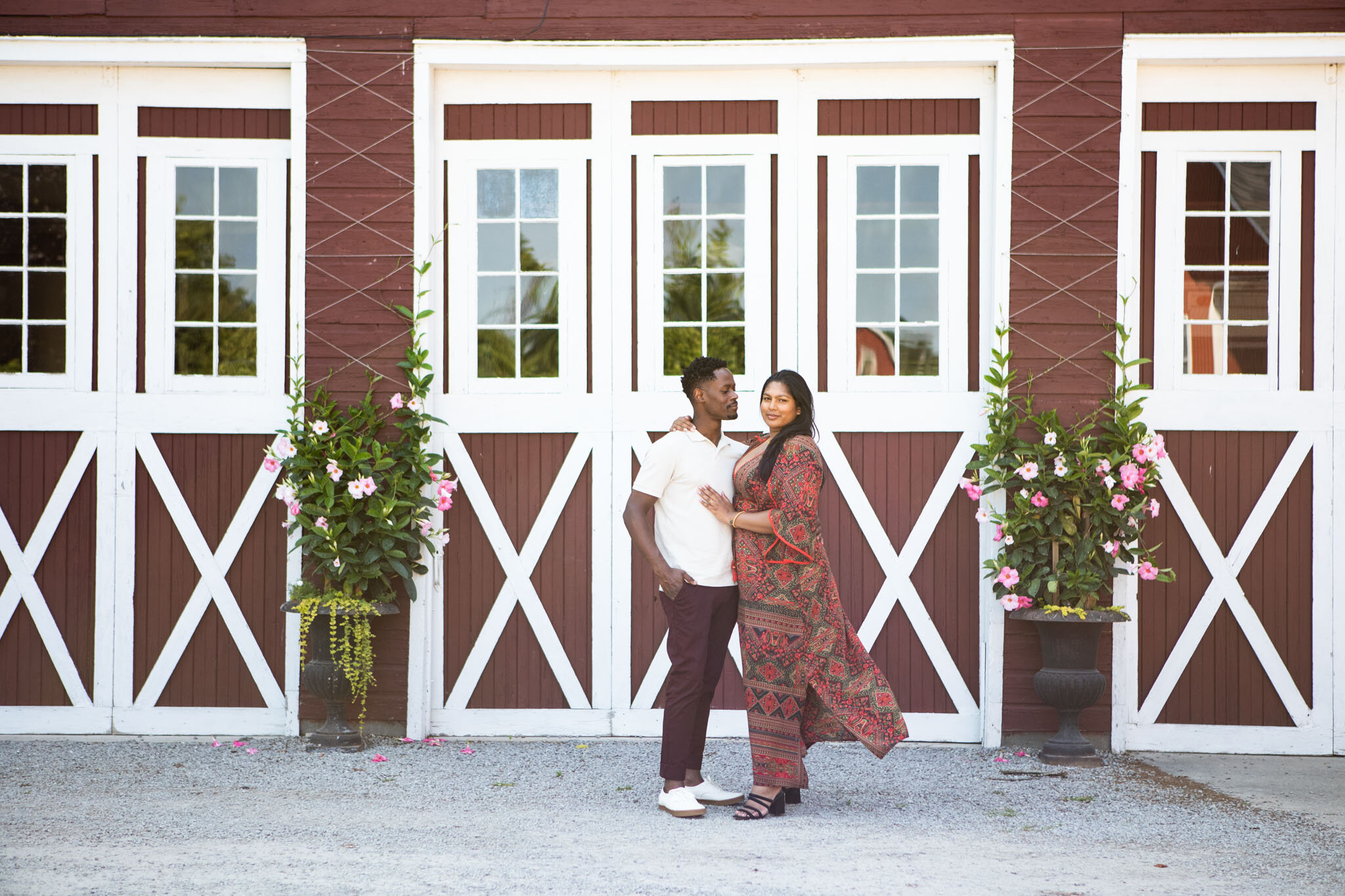 beautiful couple standing in front of a red and white barn Black man looking at his Brown female partner at Cherry Avenue Farms.jpg