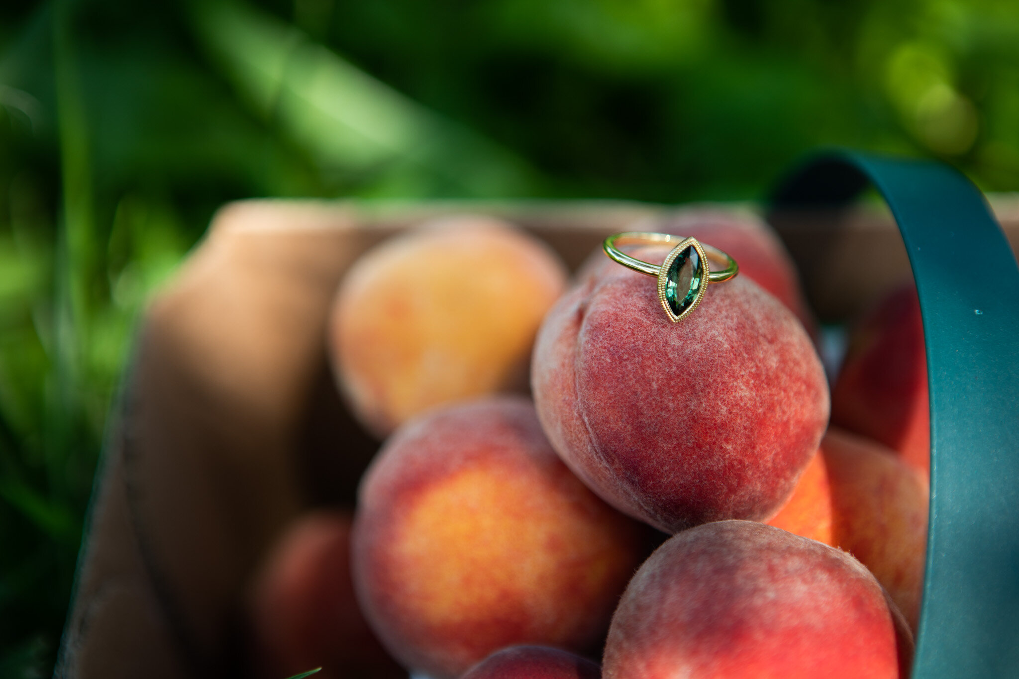 custom engagement ring with green stone sitting on a pile of peaches at Cherry Avenue Farm.jpg