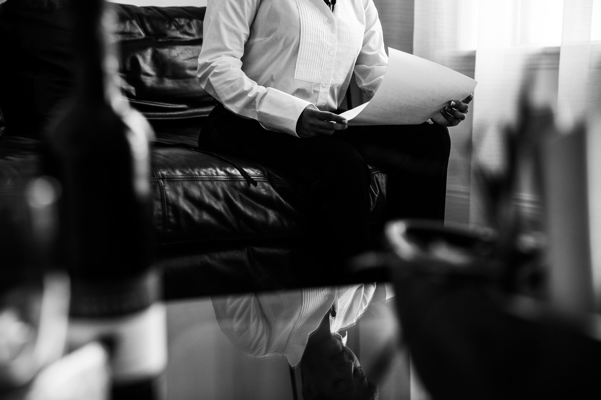 bride reading letter from future wife on wedding day in black and white with a reflection in glass coffee table.jpg