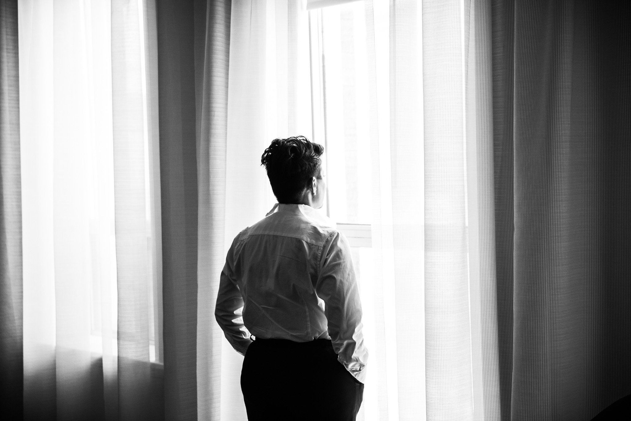 bride wearing suit looking out room window in the Walper Hotel photo in black and white.jpg