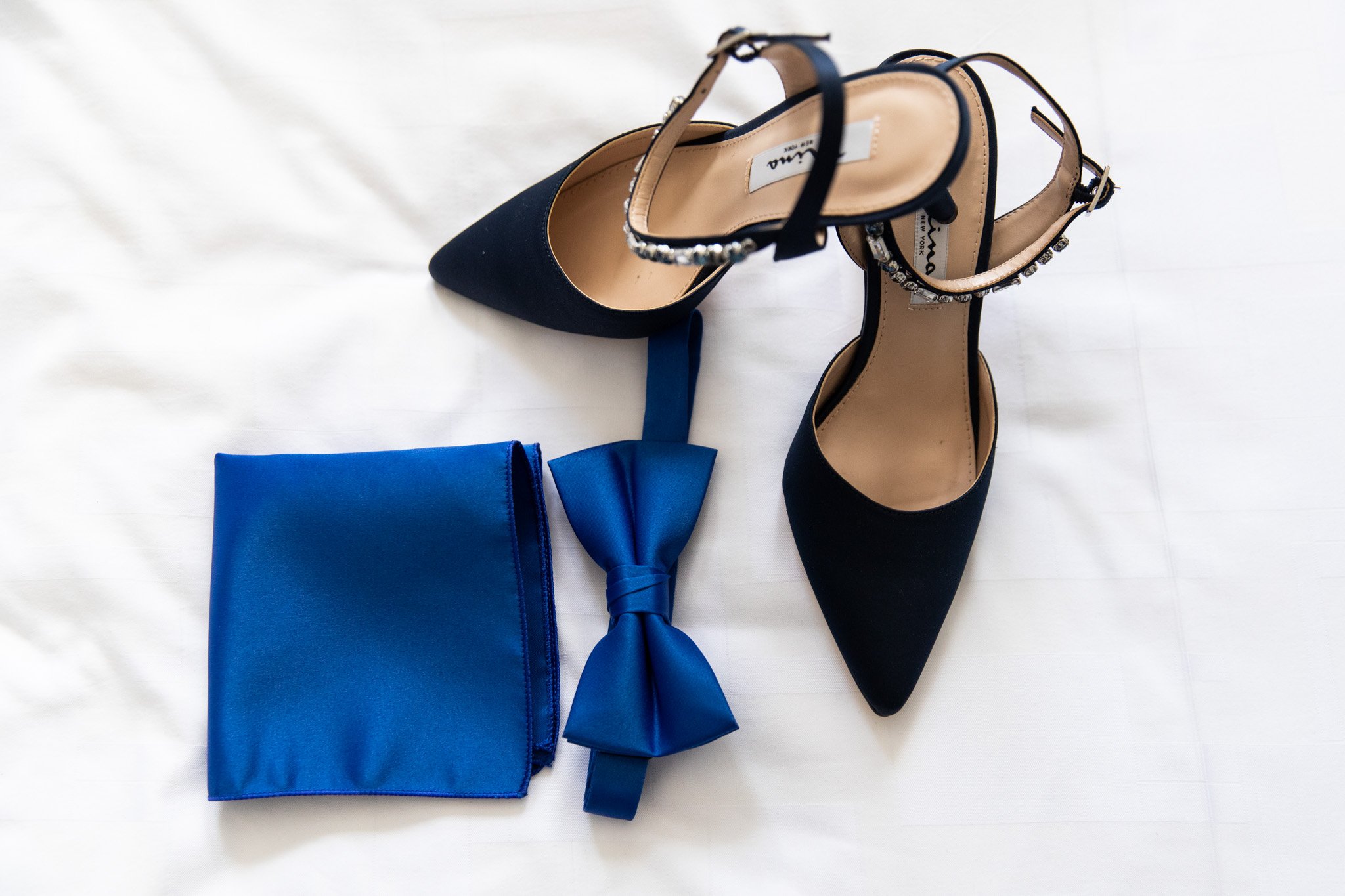 bride's black heels with blue bow tie and pocket square on a white bed at The Walper Hotel.jpg