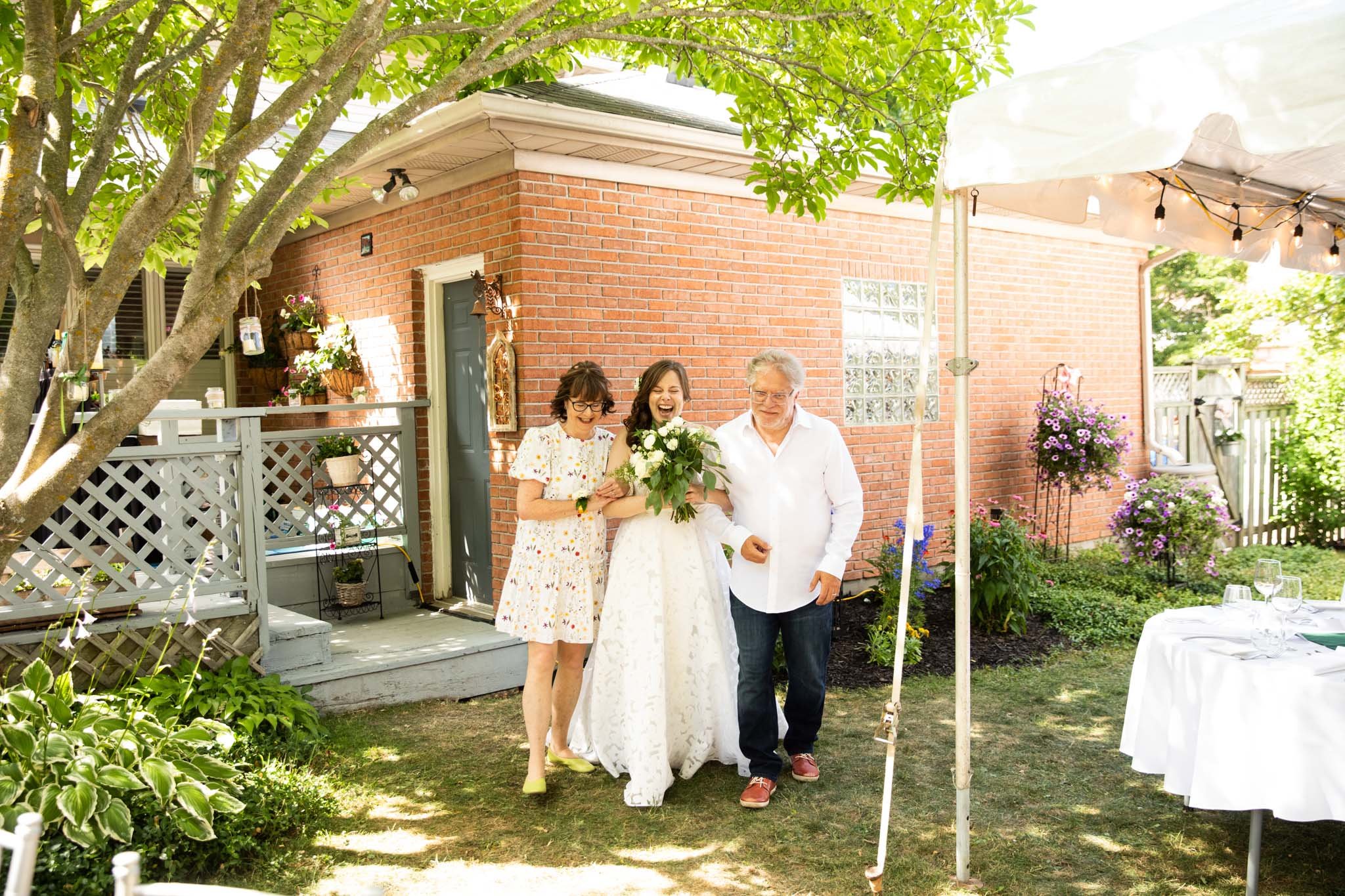 bride walking down the aisle with parents in backyard wedding.jpg