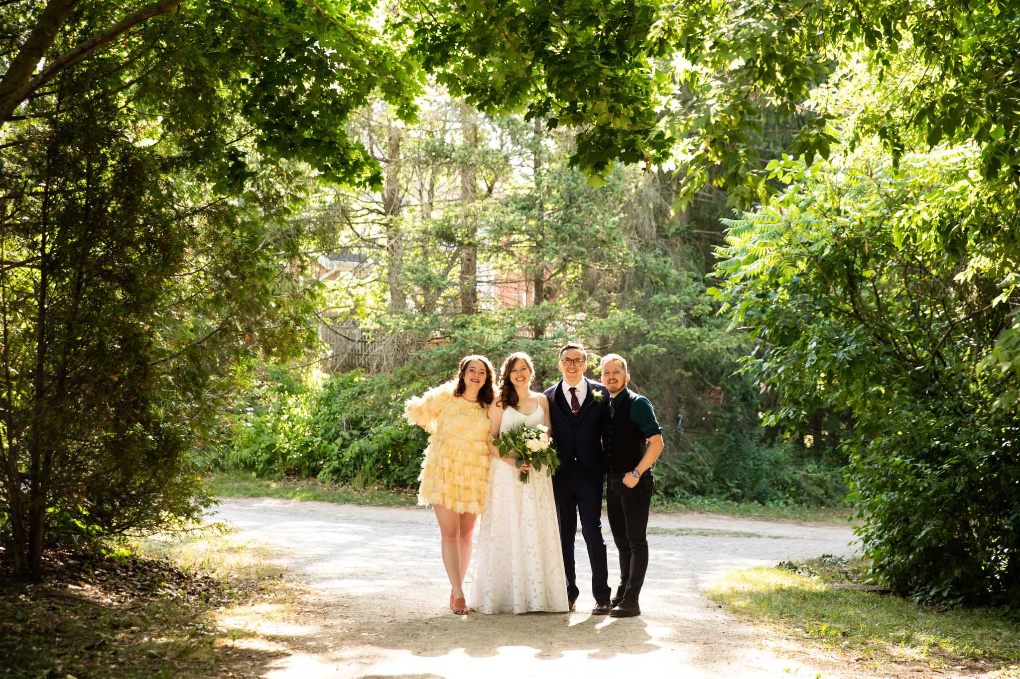 full body image of wedding party backlit and framed by trees on a path in a park.jpg