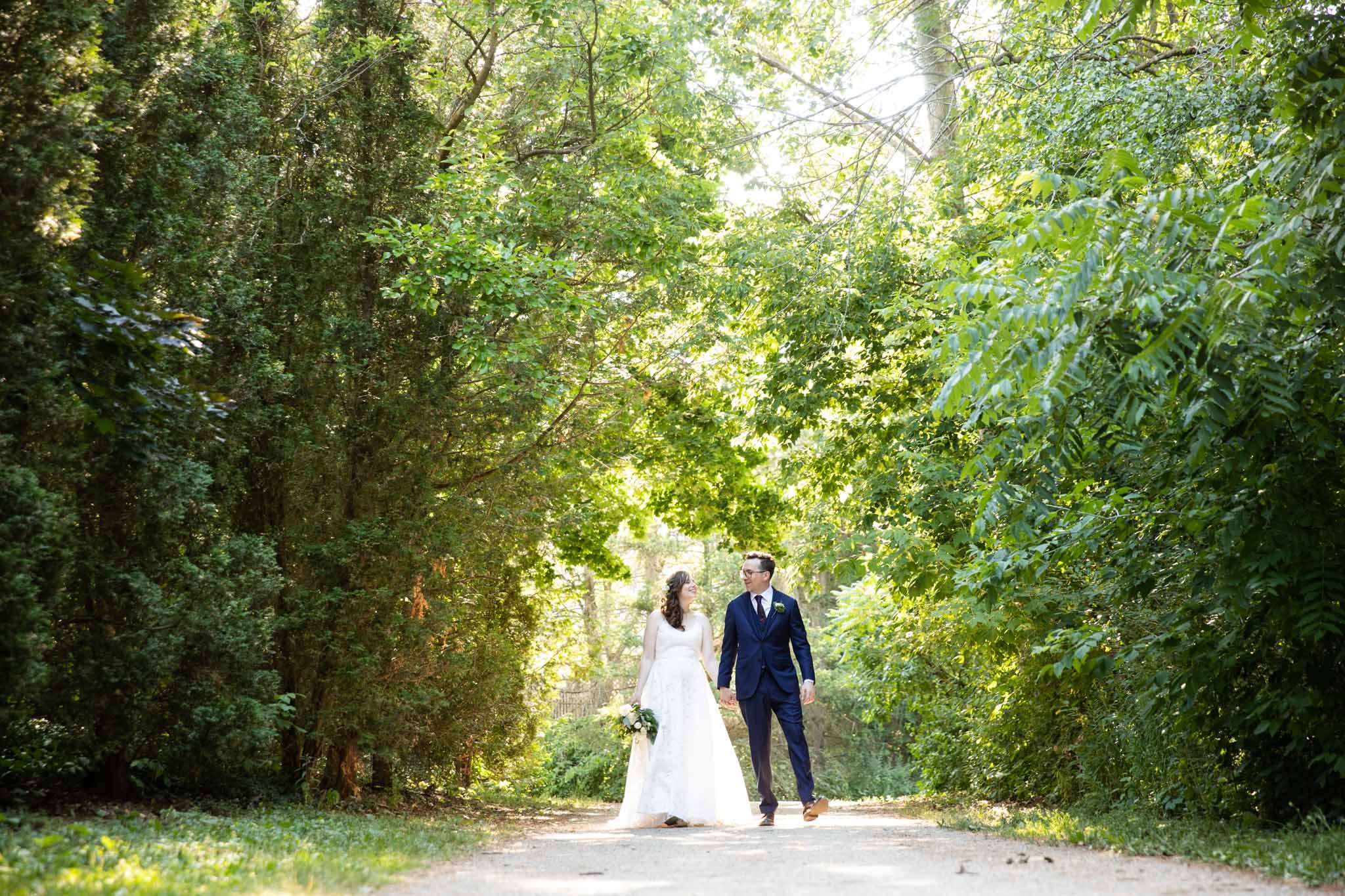 wedding couple holding hands walking on a path in a park.jpg