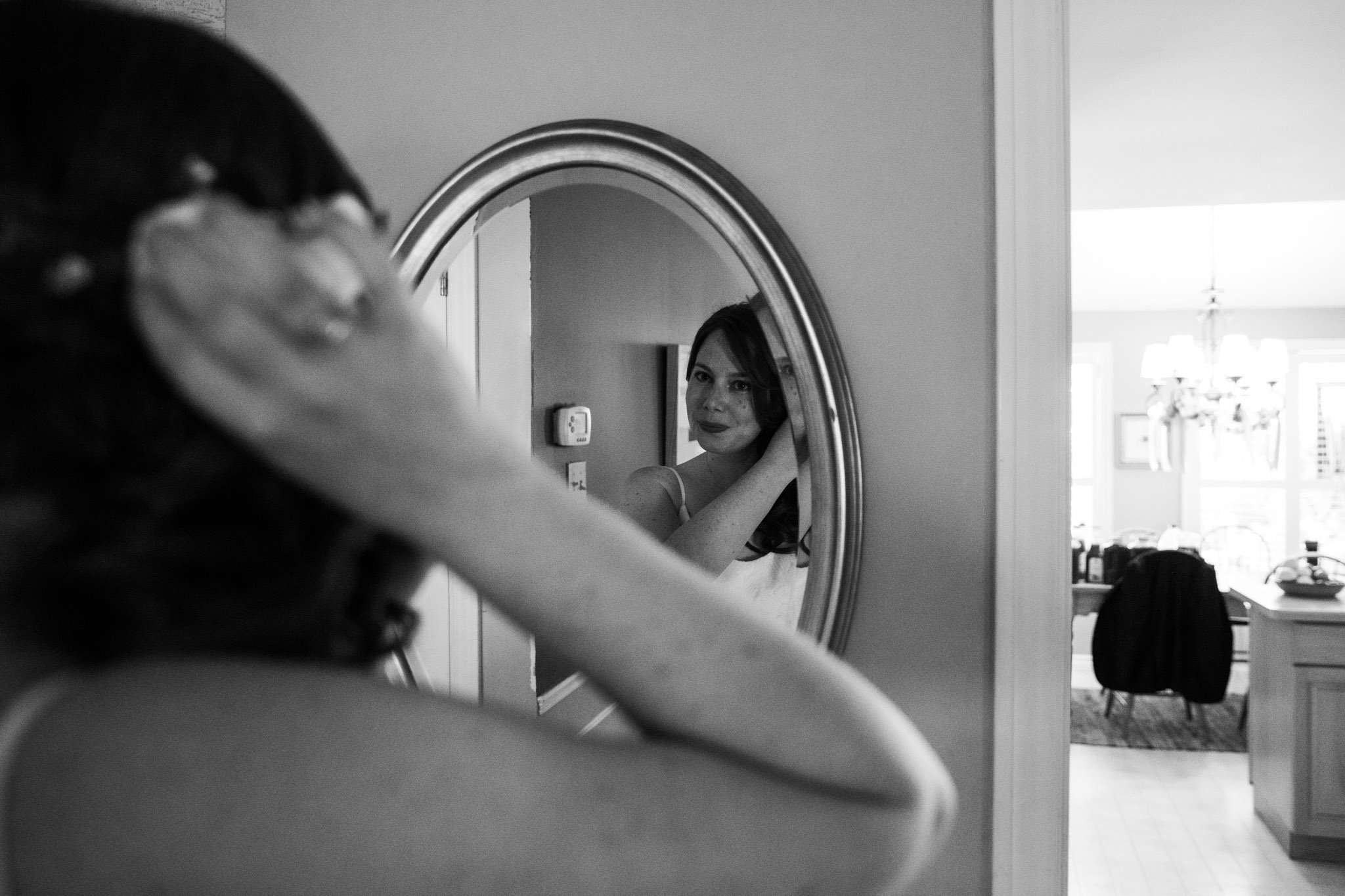 bride fixing hair reflected in oval mirror - black and white wedding photography.jpg