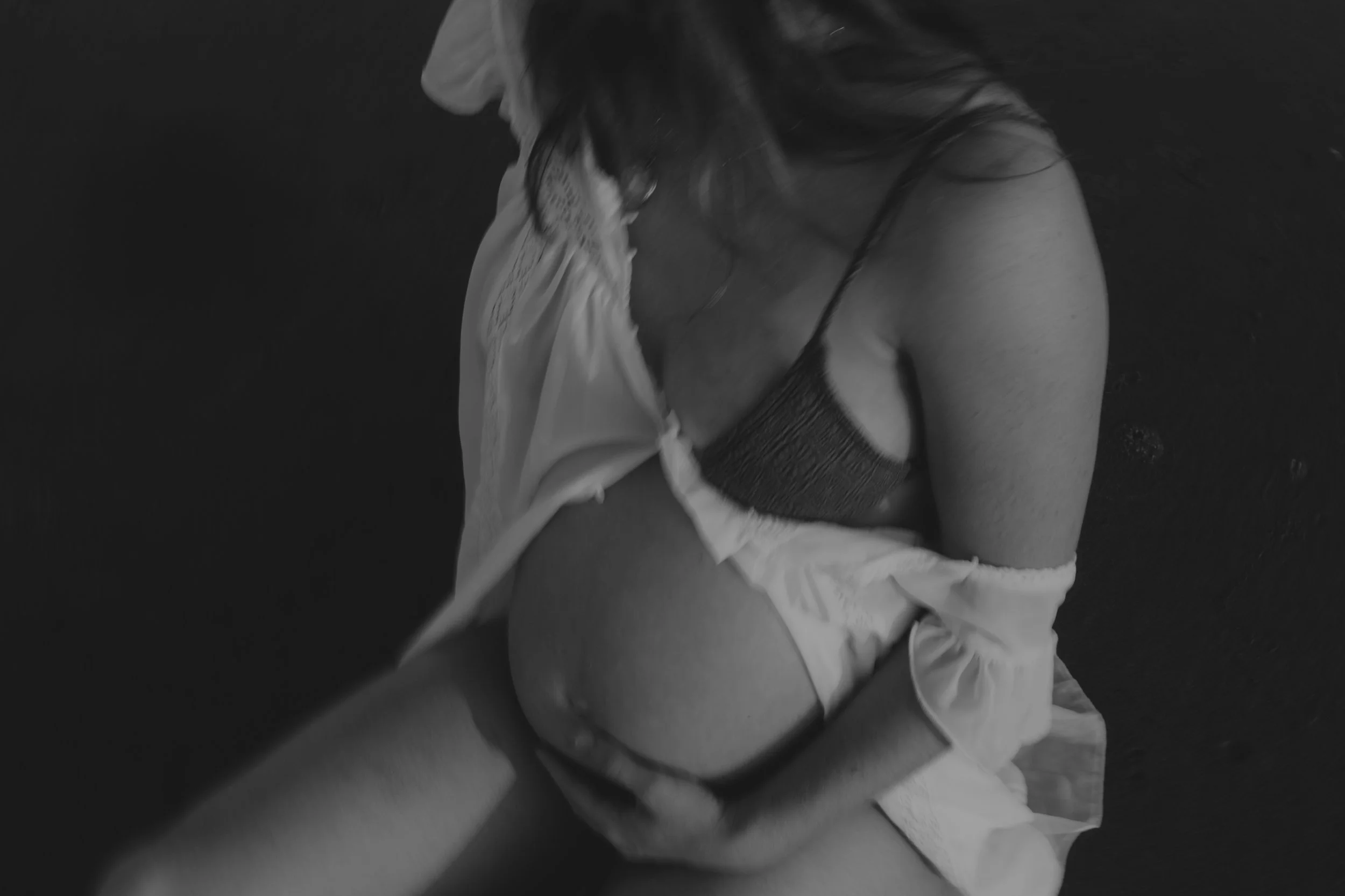 Black and white photo of a person with long hair, partially covered by a shirt, wearing a patterned bra, sitting on the floor.