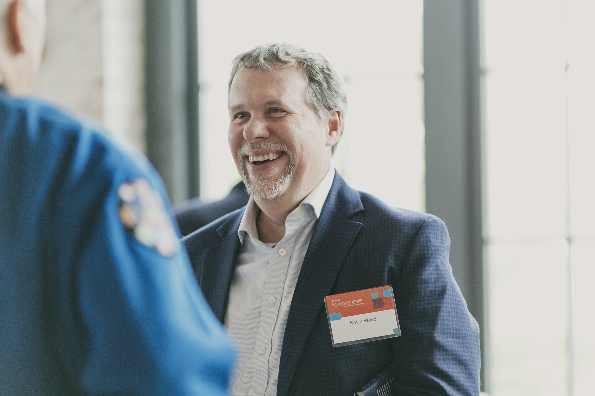 Guest in a navy blazer laughing with the astronaut during cocktail hour at a corporate speaker event
