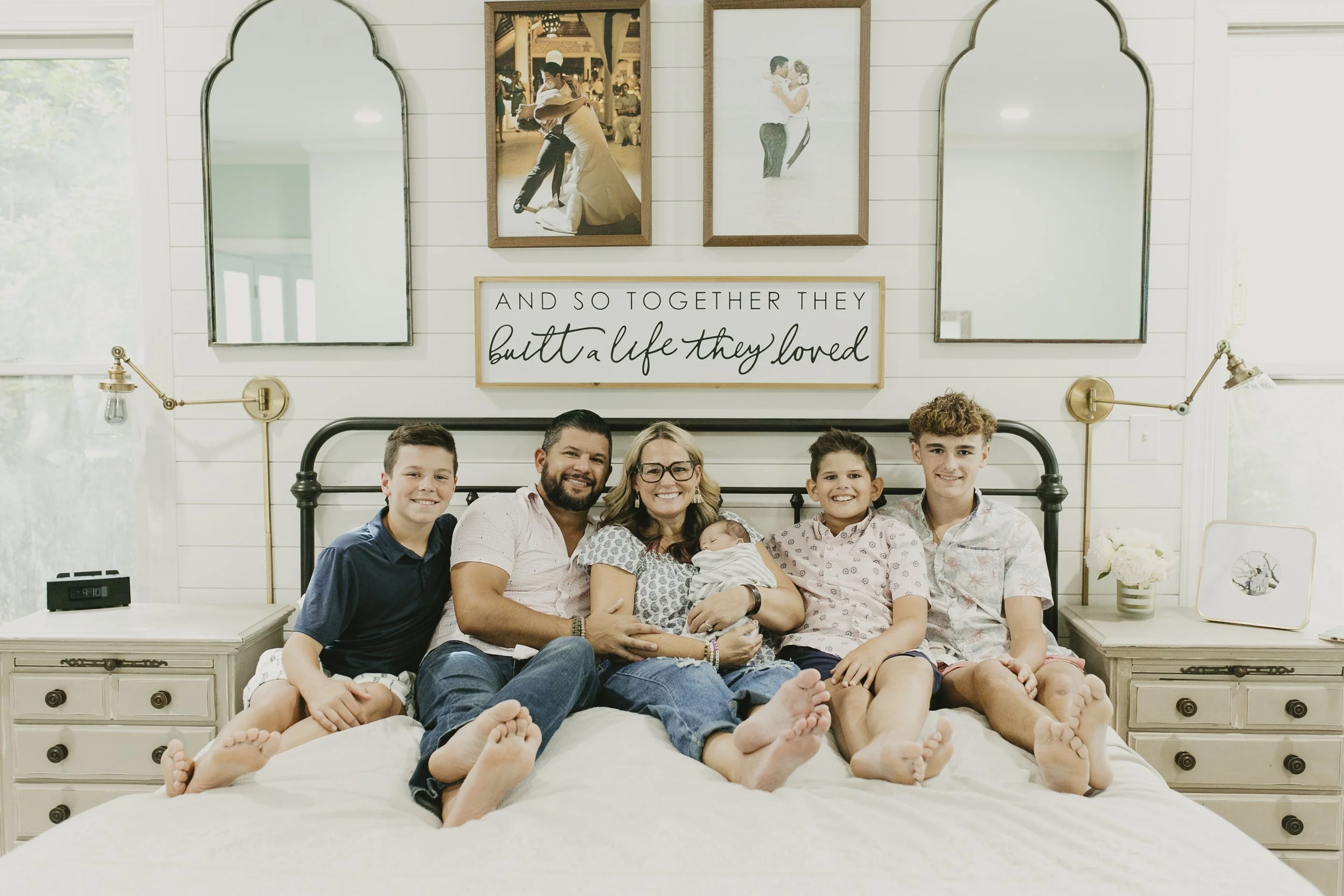 Family of six, including three older brothers, sitting together on a bed with their newborn baby during an in-home family and newborn session
