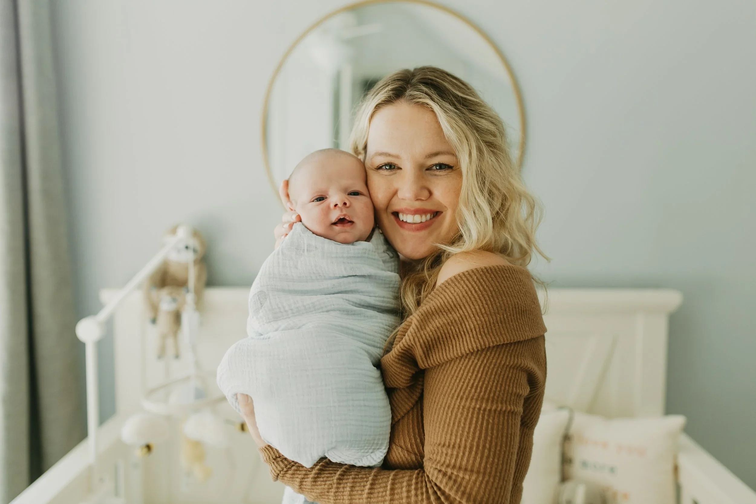 Mom smiling and holding her swaddled newborn during an in-home newborn session in a Charleston nursery