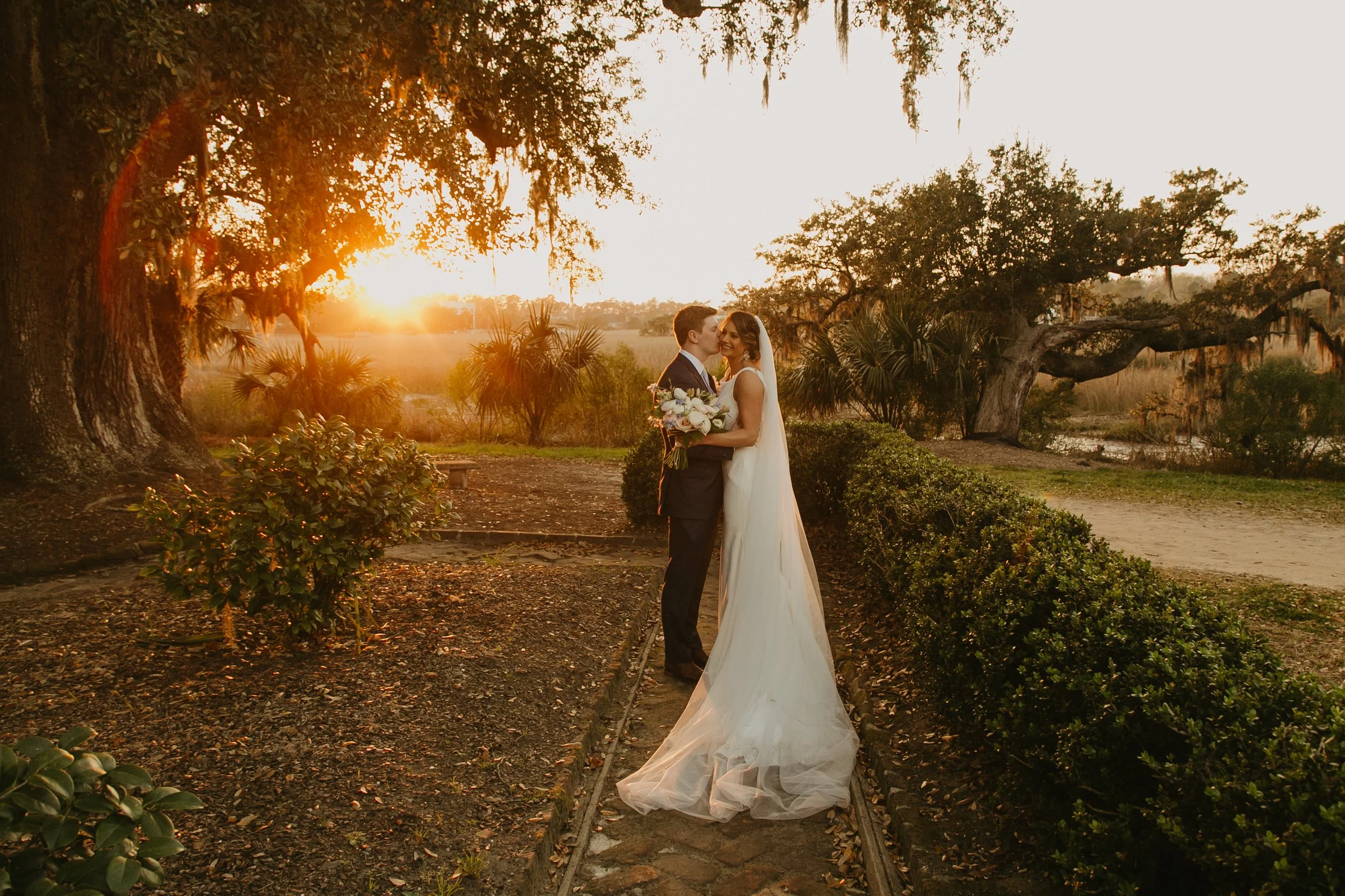 Bride and groom kissing at sunset under oak trees