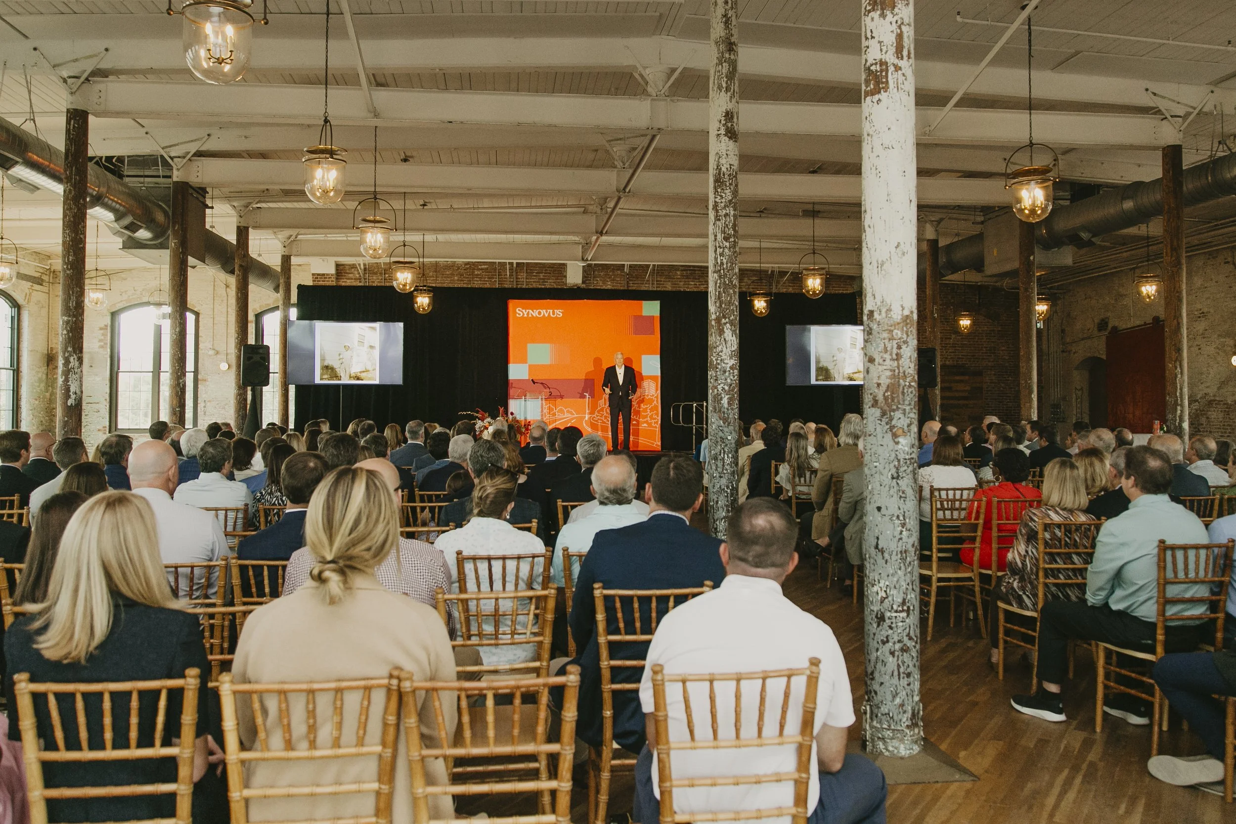 Audience listening to a keynote speaker in a historic brick mill event venue