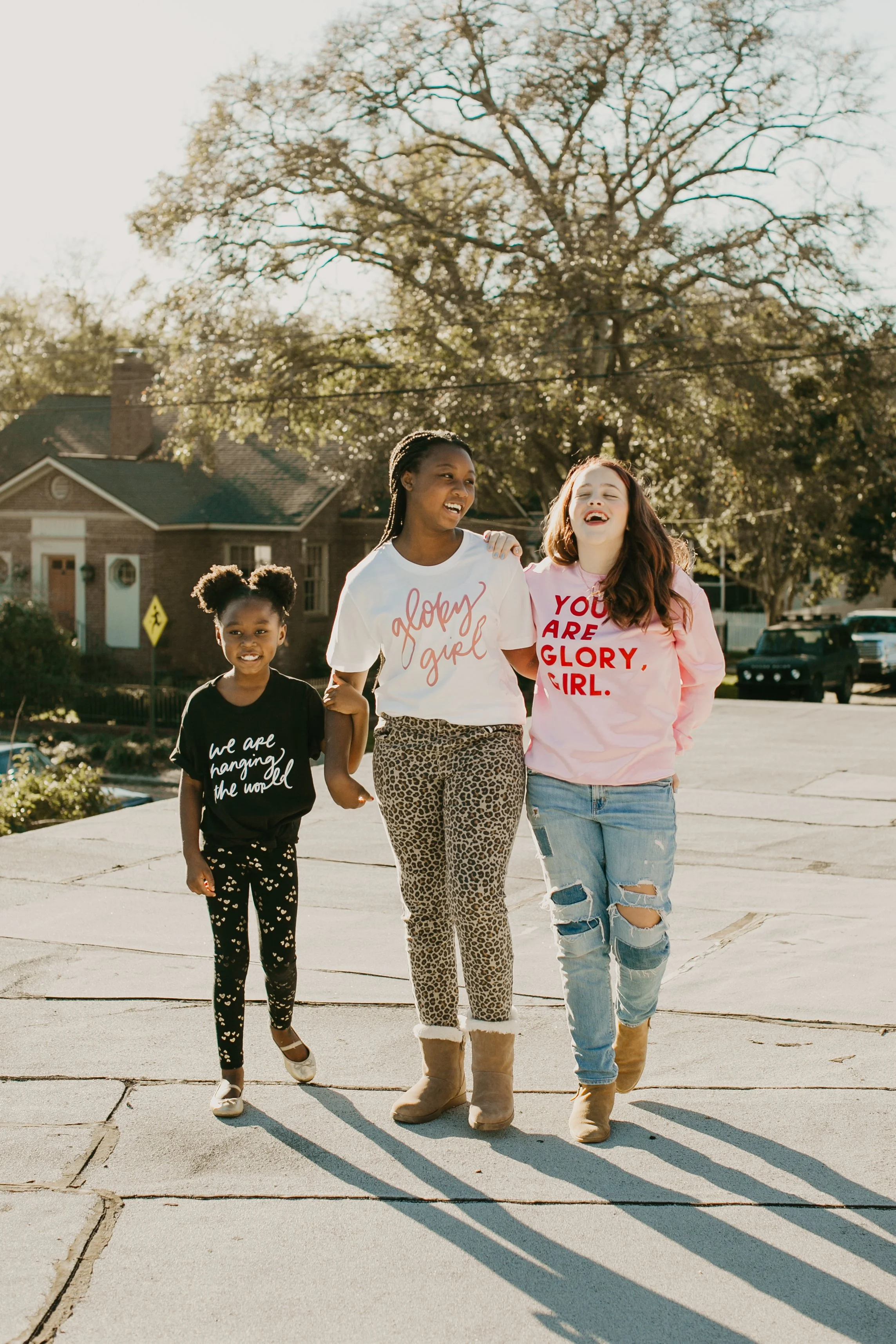 Three girls walking together in Glory Girl tees under a big oak tree at golden hour