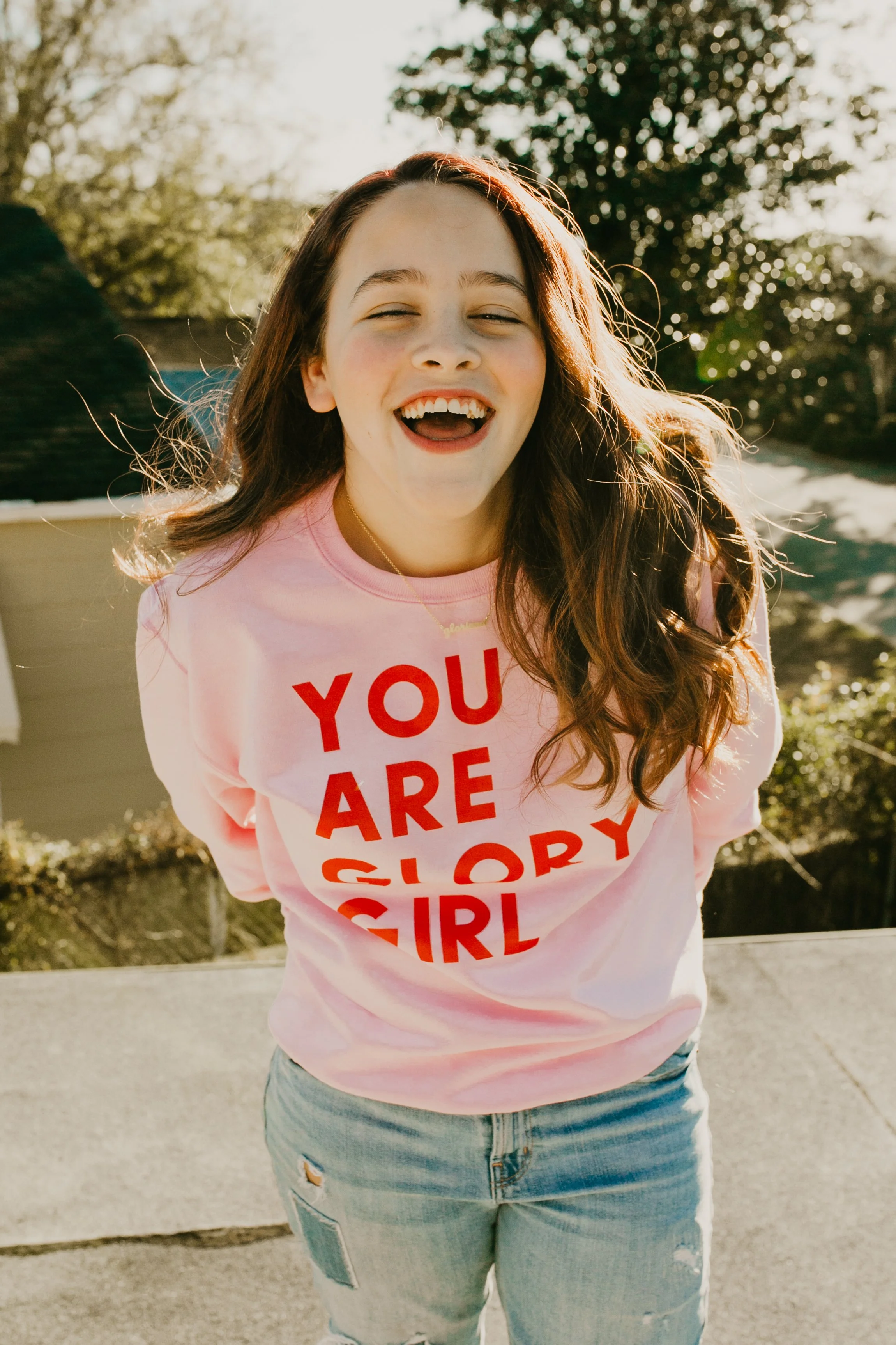 Girl laughing in a pink You Are Glory Girl sweatshirt during a Glory Girl brand photo session
