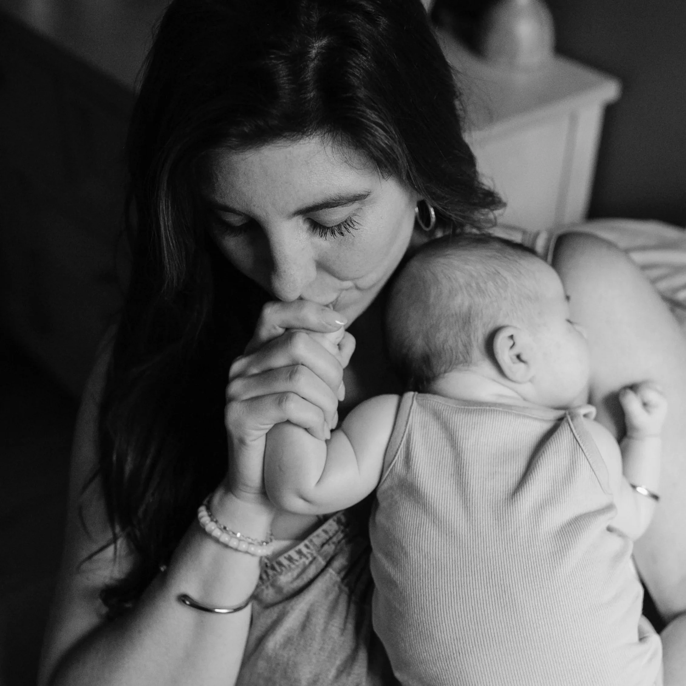 Mom kissing her newborn's tiny hand during an in-home newborn session in Charleston