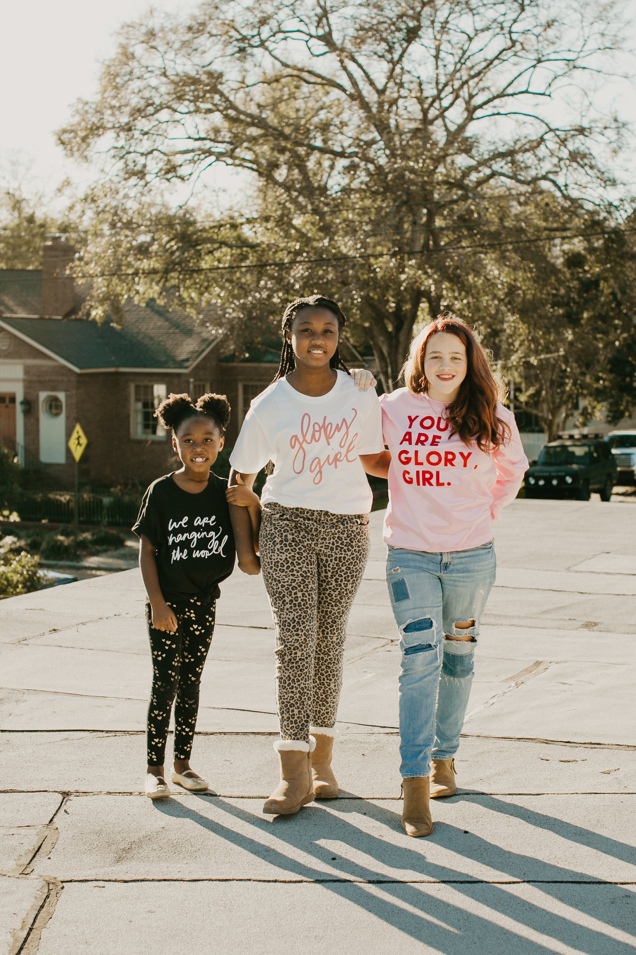 Three girls walking down a tree lined street in Glory Girl tees during a brand photo session