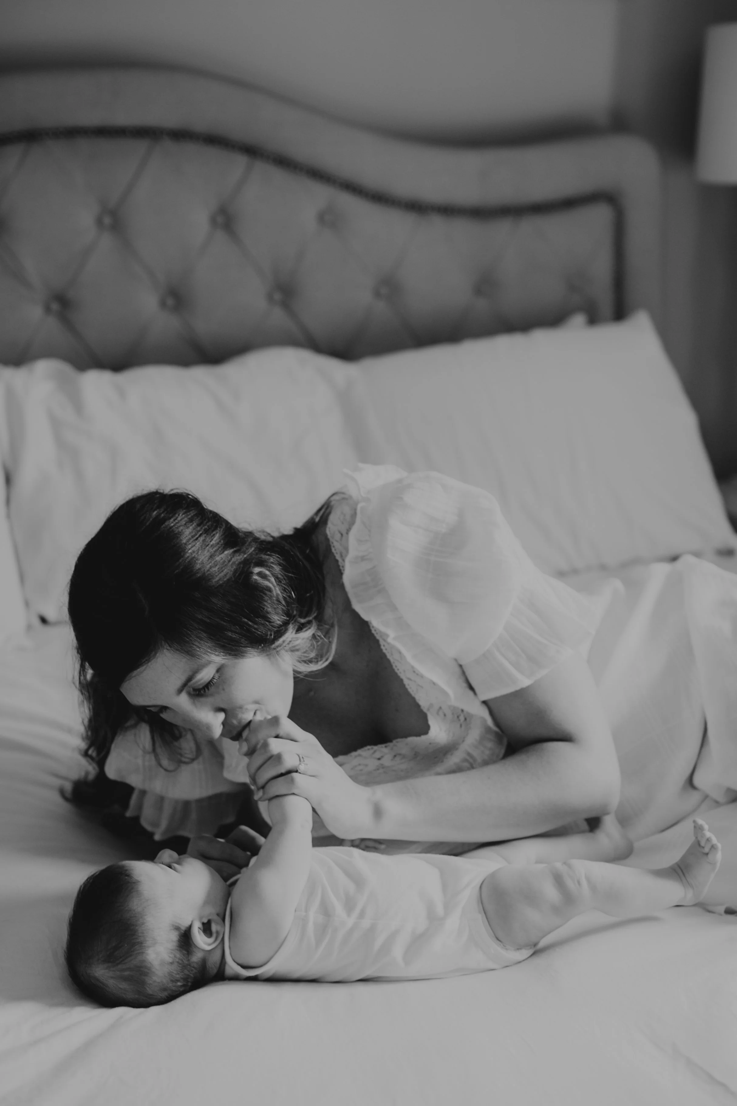 A woman and child lying on a bed, holding hands, with the woman kissing the child's hand.
