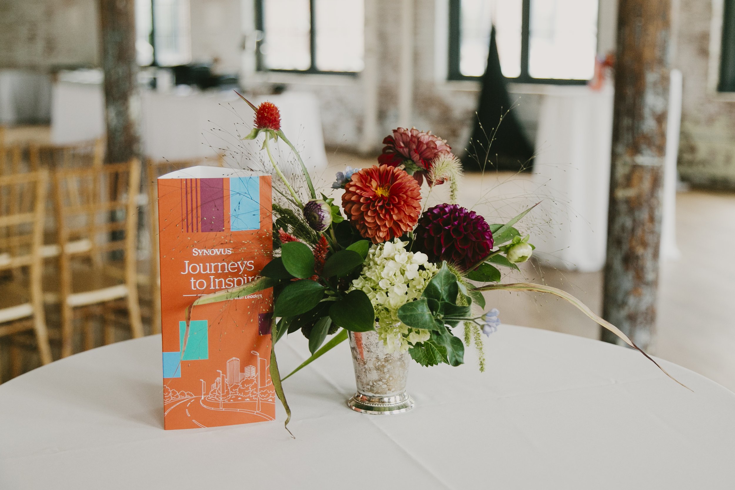 Event program and dahlia centerpiece on a cocktail table at a corporate speaker event