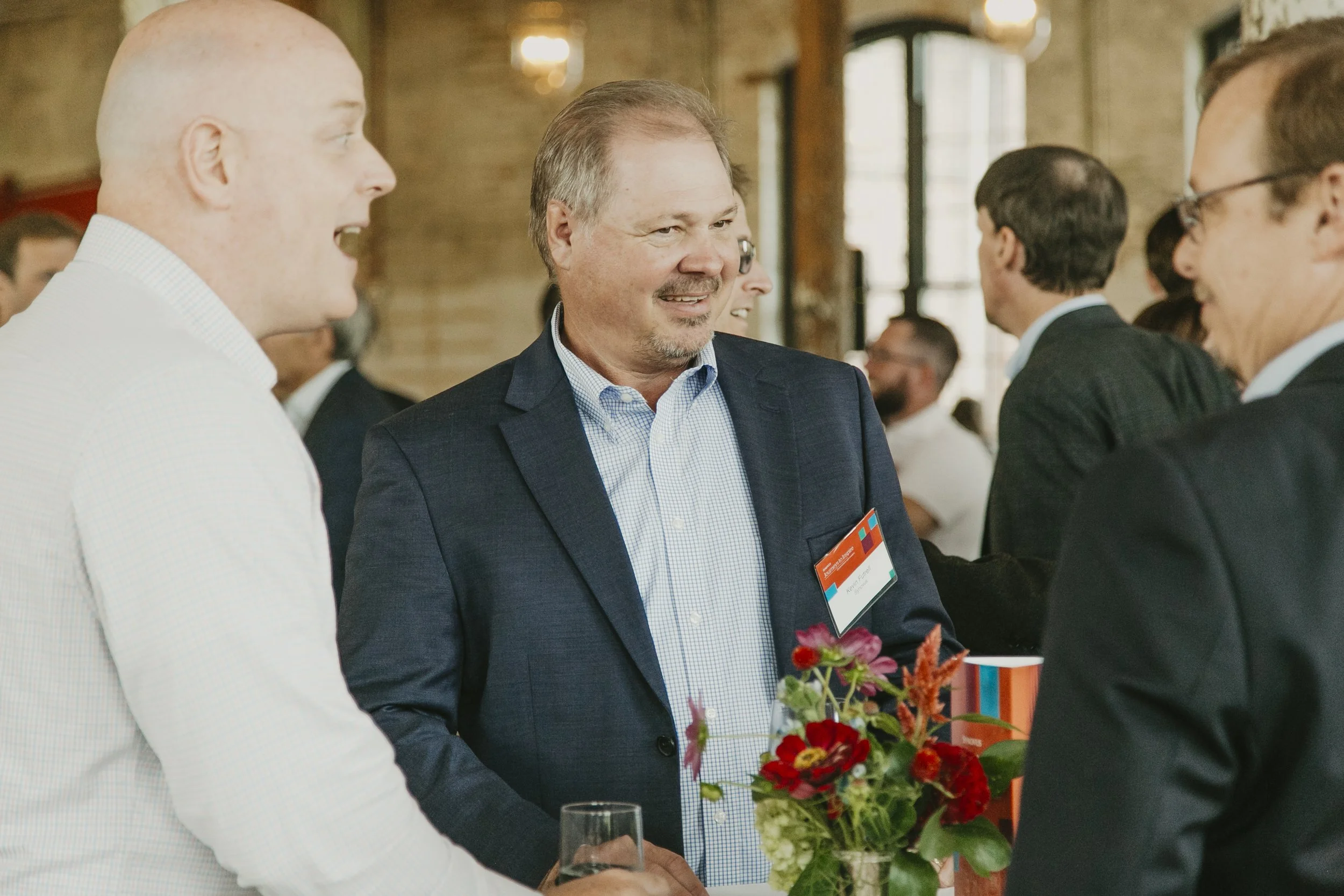 Guests chatting over drinks by a floral centerpiece during the Synovus Journeys to Inspire reception