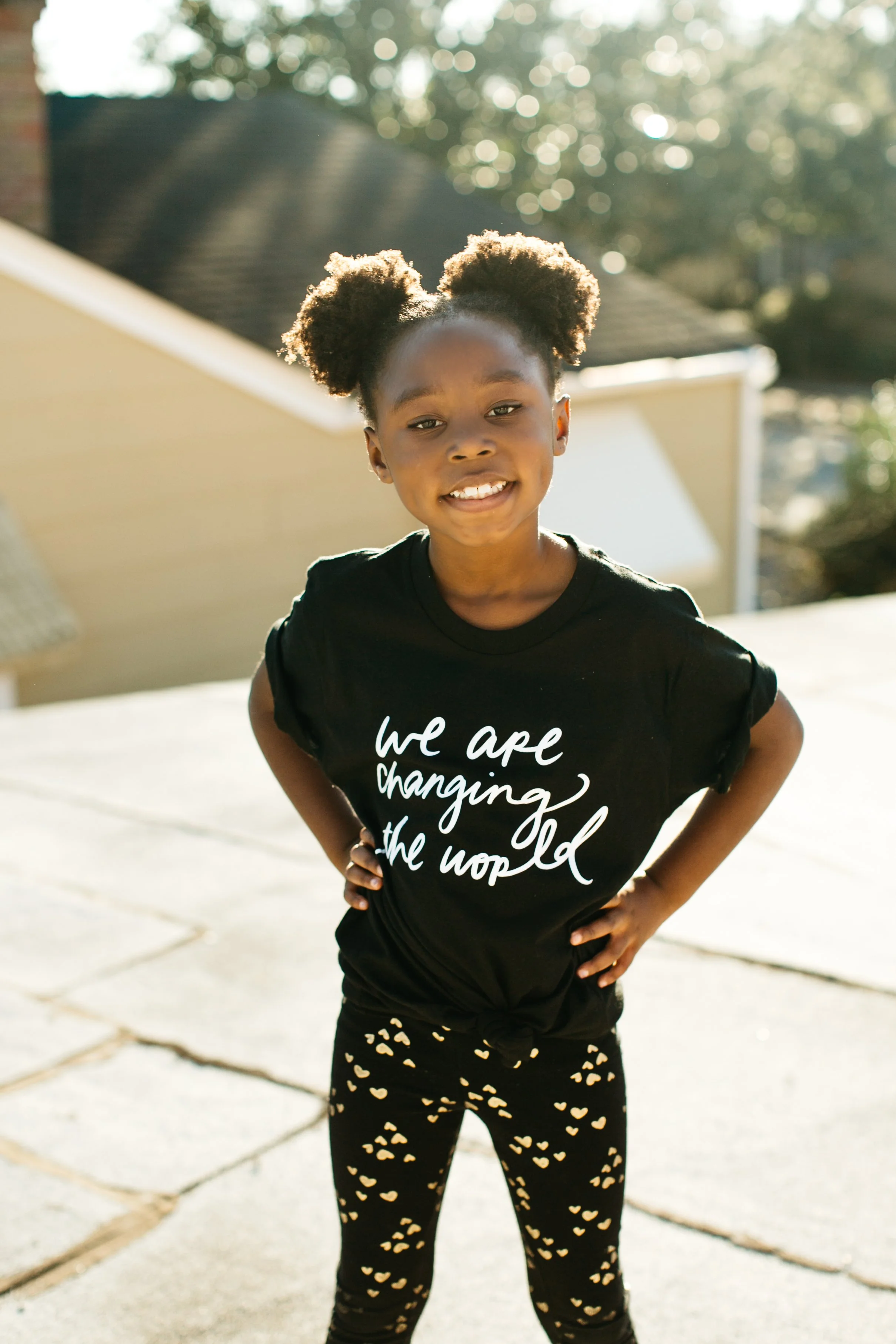 Little girl smiling with hands on her hips in a We Are Changing the World tee for a Glory Girl brand shoot