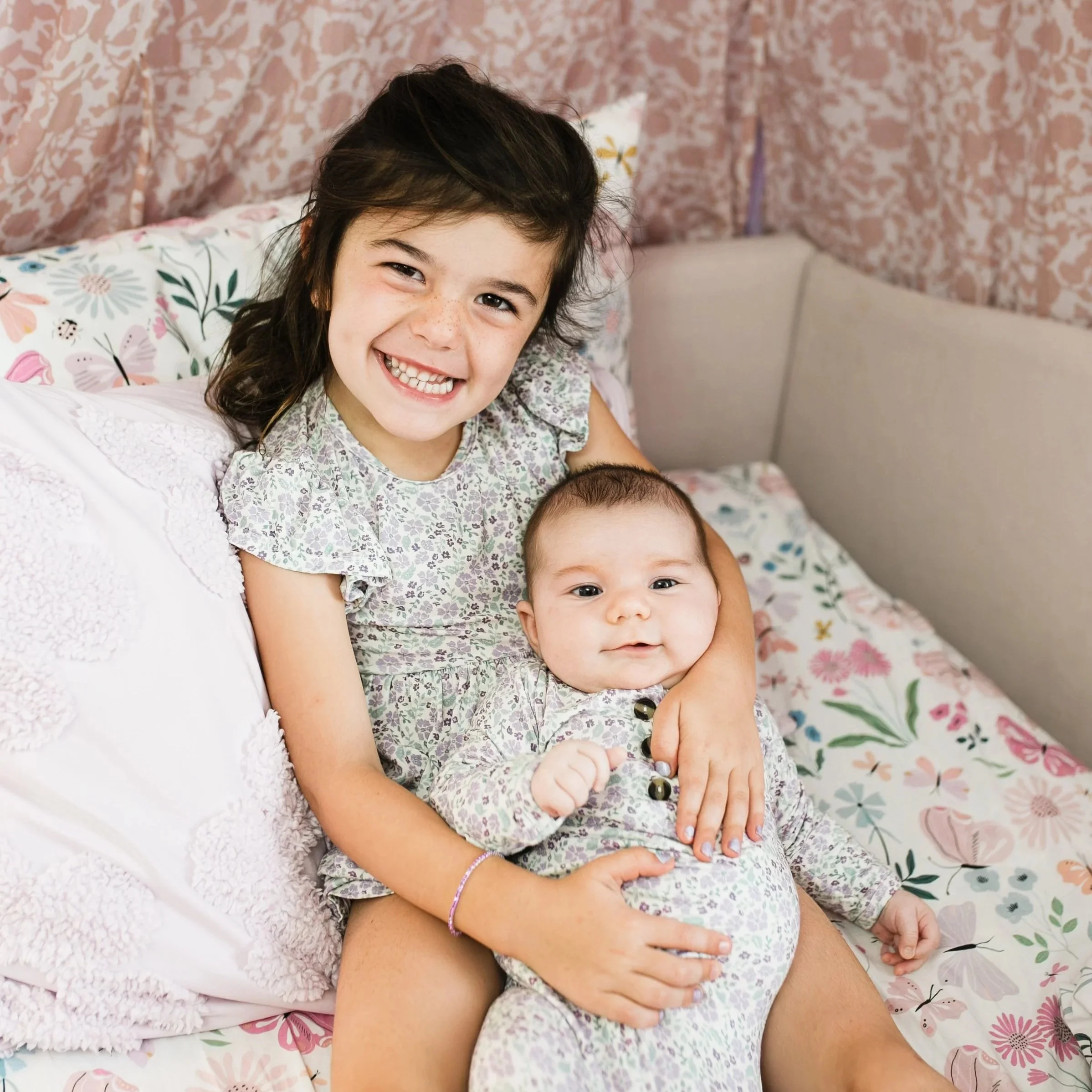 Big sister smiling on the bed next to the bassinet during an in-home newborn session in Charleston