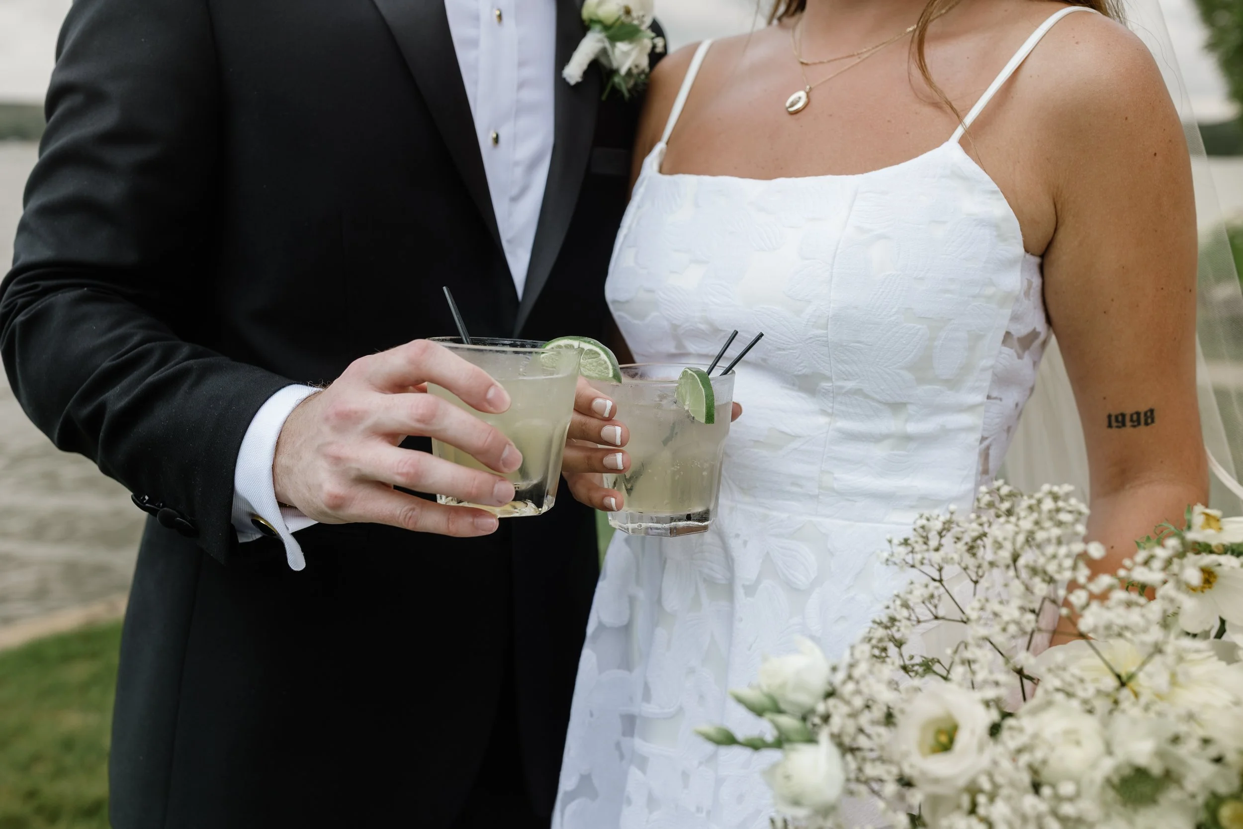 Close-up of a bride and groom holding drinks with lime wedges during a wedding celebration.