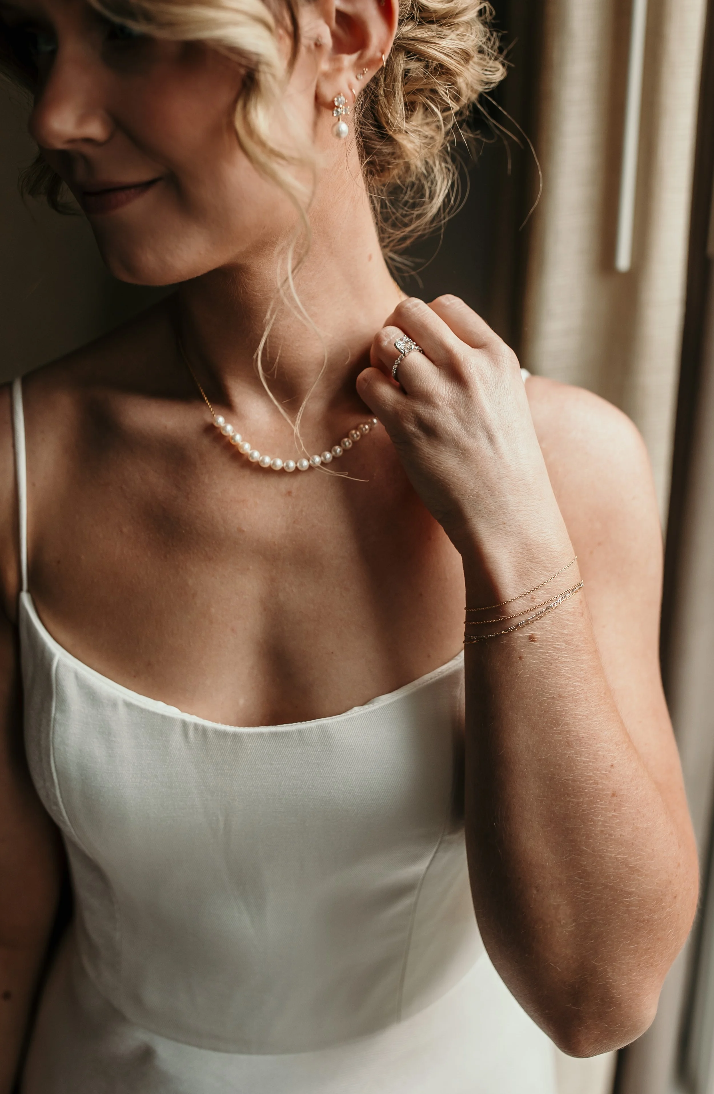 Close-up of a bride showcasing her pearl necklace, engagement ring, and delicate gold bracelets, highlighting elegant bridal details.
