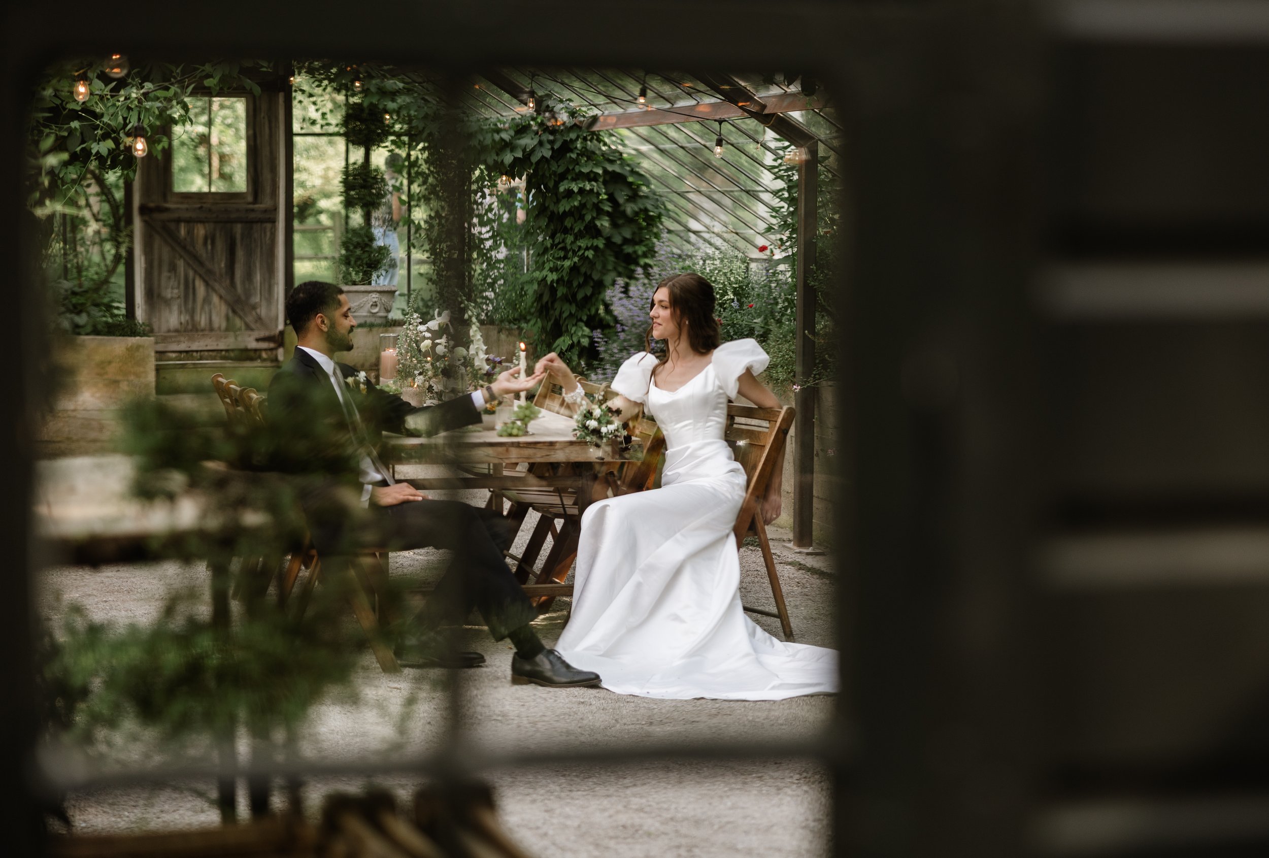 A bride and an older man, possibly her father, standing together in front of a large window with curtains. The bride is visibly emotional, wiping her tears, while the man looks at her with a gentle smile. The scene appears to be in a well-lit room with ornate wall sconces and patterned furniture.