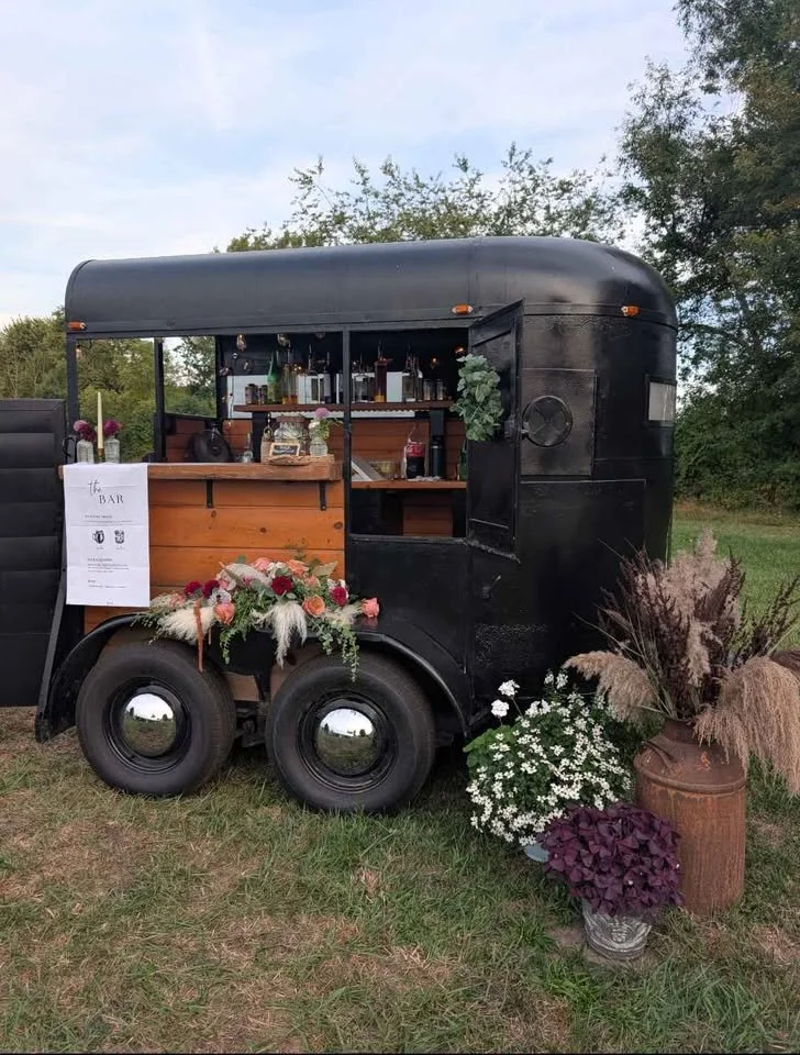 Black vintage trailer used as a mobile bar with flowers and a menu displayed outside