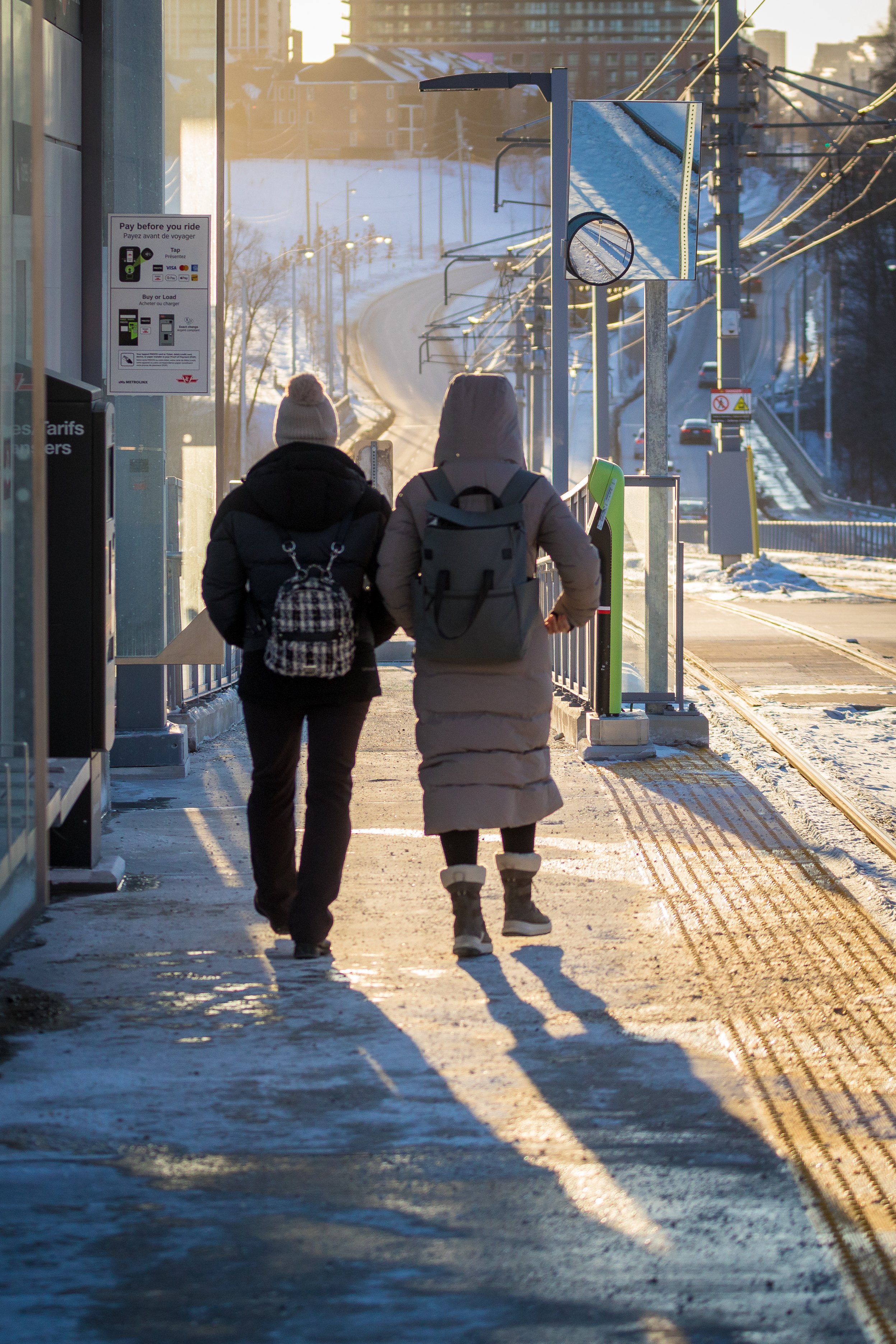  Two riders walk away from the platform at sunset on the opening day of the Eglinton Crosstown LRT, their shadows stretching across the station as the new line settles into everyday use.  