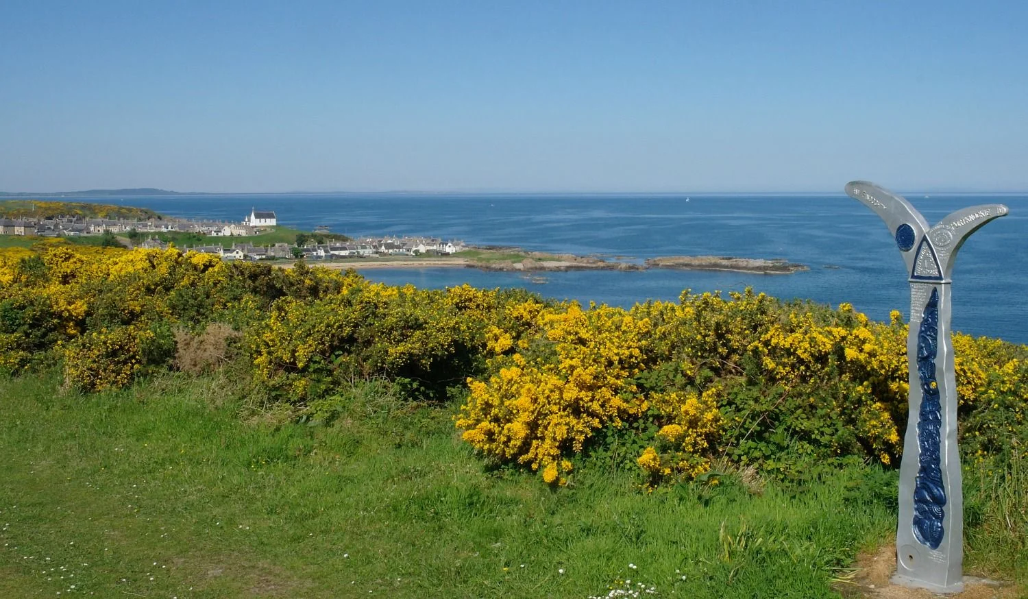 It's a grand morning in June. The Moray Firth is calm, the hills across the Firth are hazy and blue, the gorse flowers smell like coconut and only a weird coastal path indicator (on right) jars slightly. (Och, maybe you like it...) This is the coastal path section between the villages of Portknockie, to the east and (pictured distantly here) Findochty.