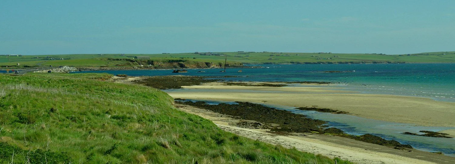 To protect the naval anchorage of Scapa Flow, the Churchill Barriers were created. End-on view of the barrier (on the left and carrying main road between St Margaret's Hope and Kirkwall) that joins Lamb Holm to Glims Holm, From where this picture was taken Lamb Holm is where the famous Italian Chapel is situated - you can't miss it. It was built by Italian POWs otherwise employed on the Churchill Barriers. Note also - centre of pic - the remains of the blockships sunk here to protect the channel before the barriers were built.