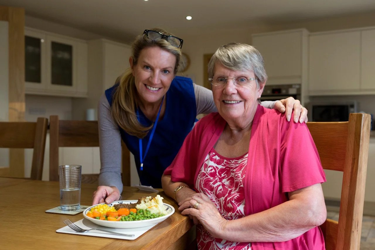 Middle-aged female caregiver setting meal in front of elderly woman