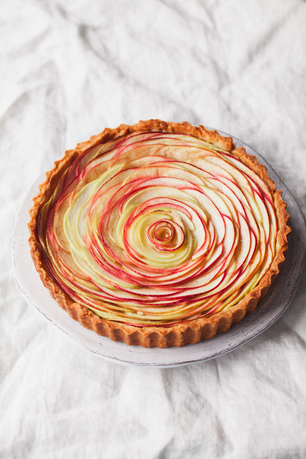 A baked apple rose tart with frangipane filling.  Apple slices are fanned around the tart to create a beautiful rose pattern.