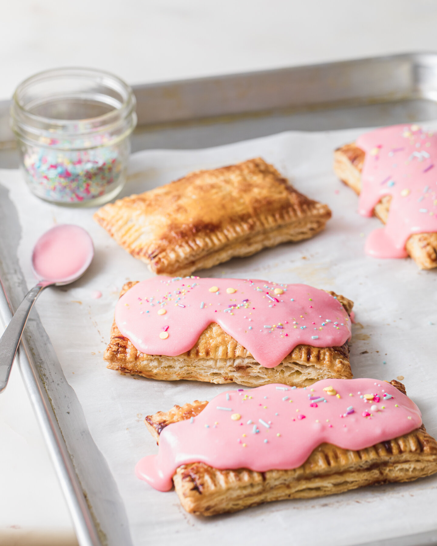 Dripping pink glaze with spinkles on top of homemade strawberry pop tarts on a baking sheet.