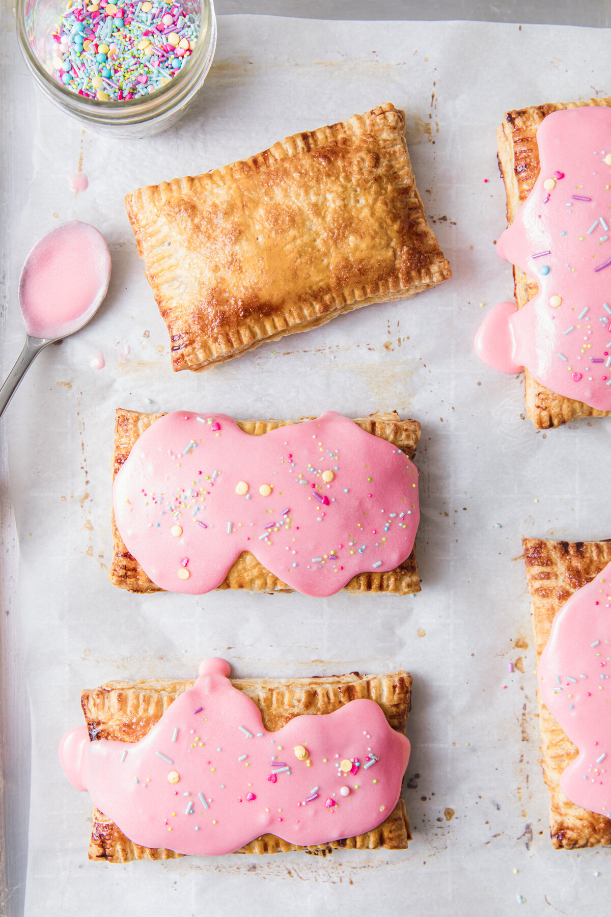 Homemade Strawberry Pop Tarts being glazed wtih pink frosting on a baking sheet.