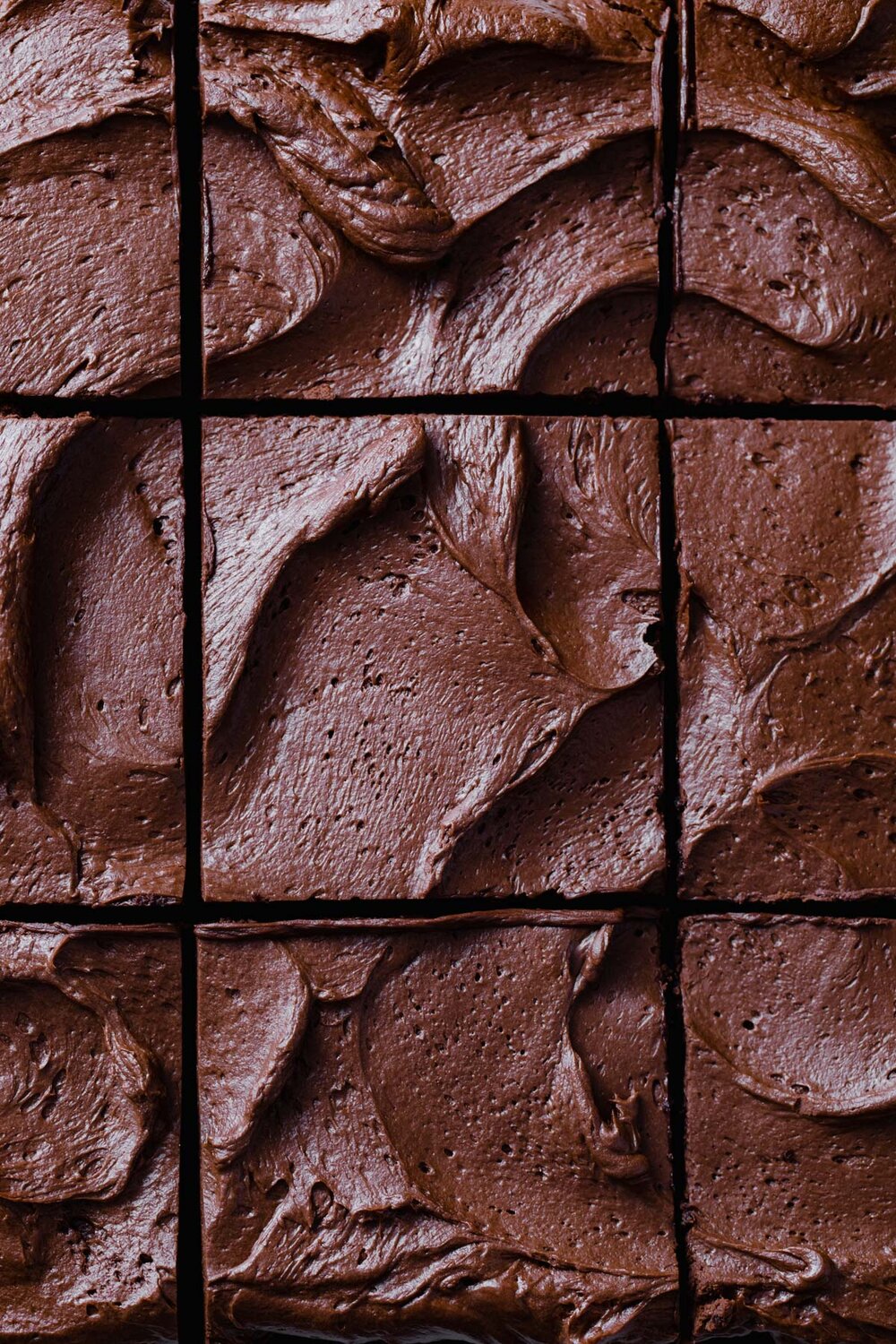 A close-up photo of swirls of whipped chocolate ganache on a sliced chocolate sheet cake