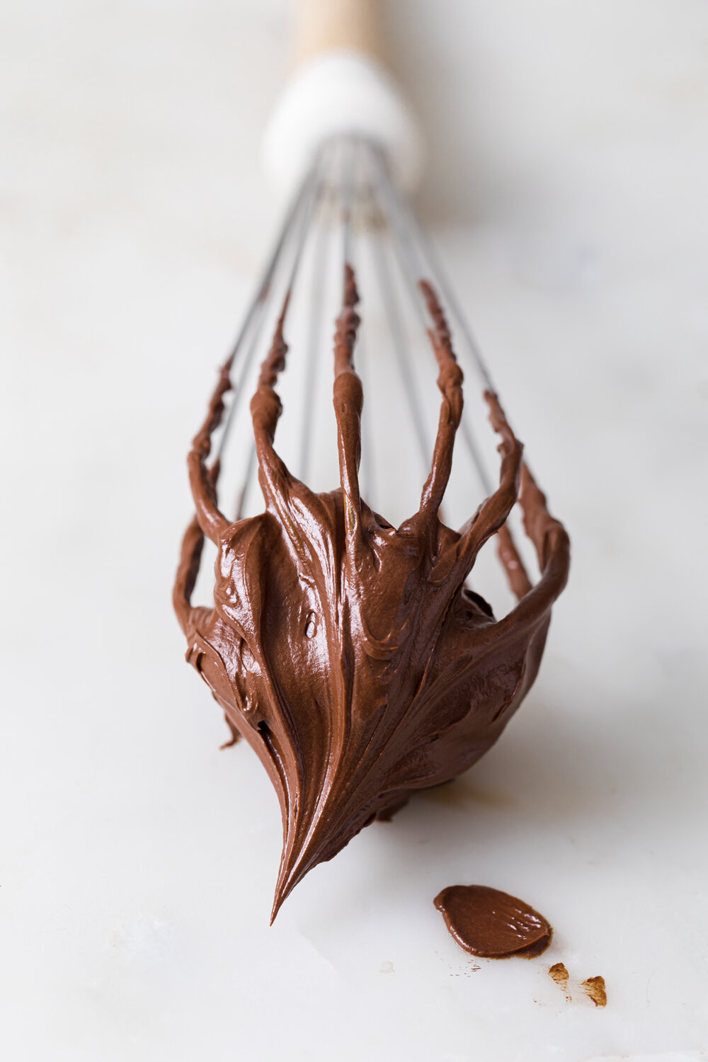 A close-up picture of a whisk covered in soft peaks of whipped chocolate ganache.