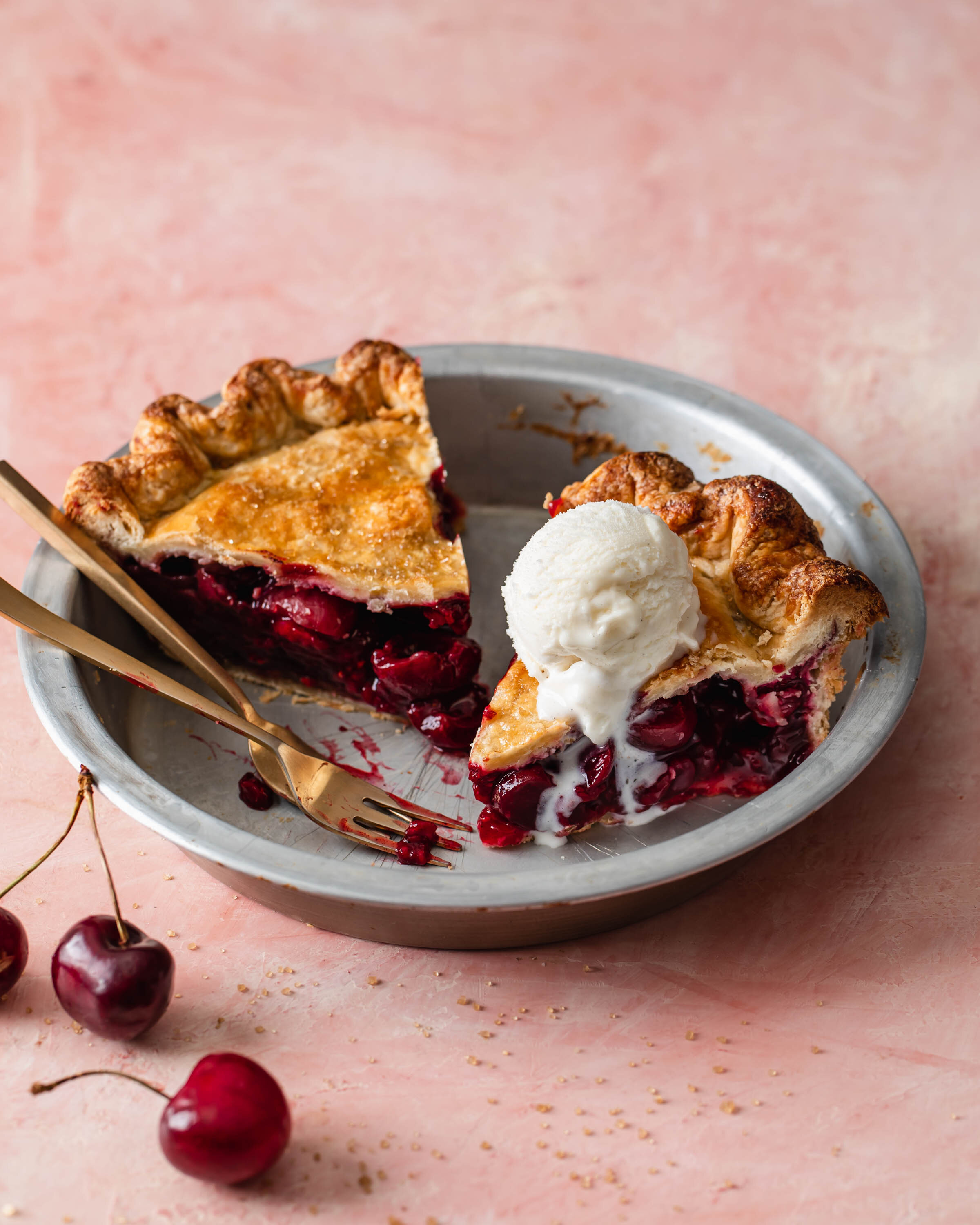 Homemade cherry pie slices in a pie tin with a scoop of vanilla ice cream